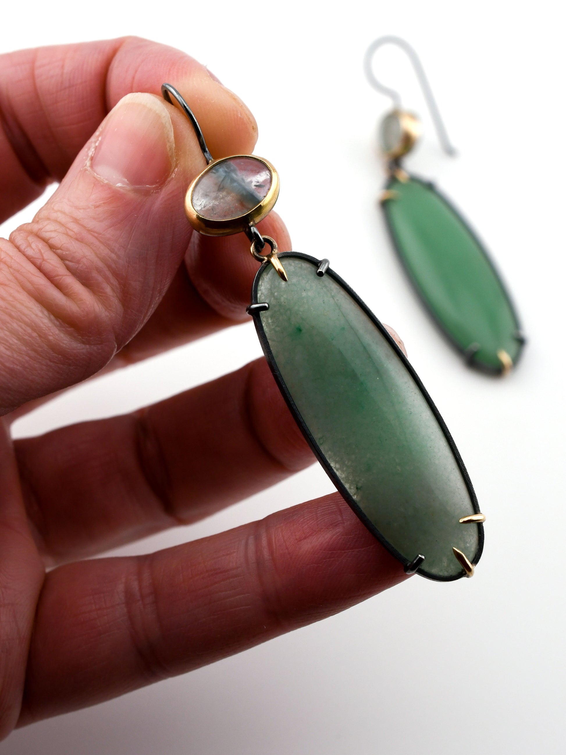 Green earrings held by a hand with a blurred background
