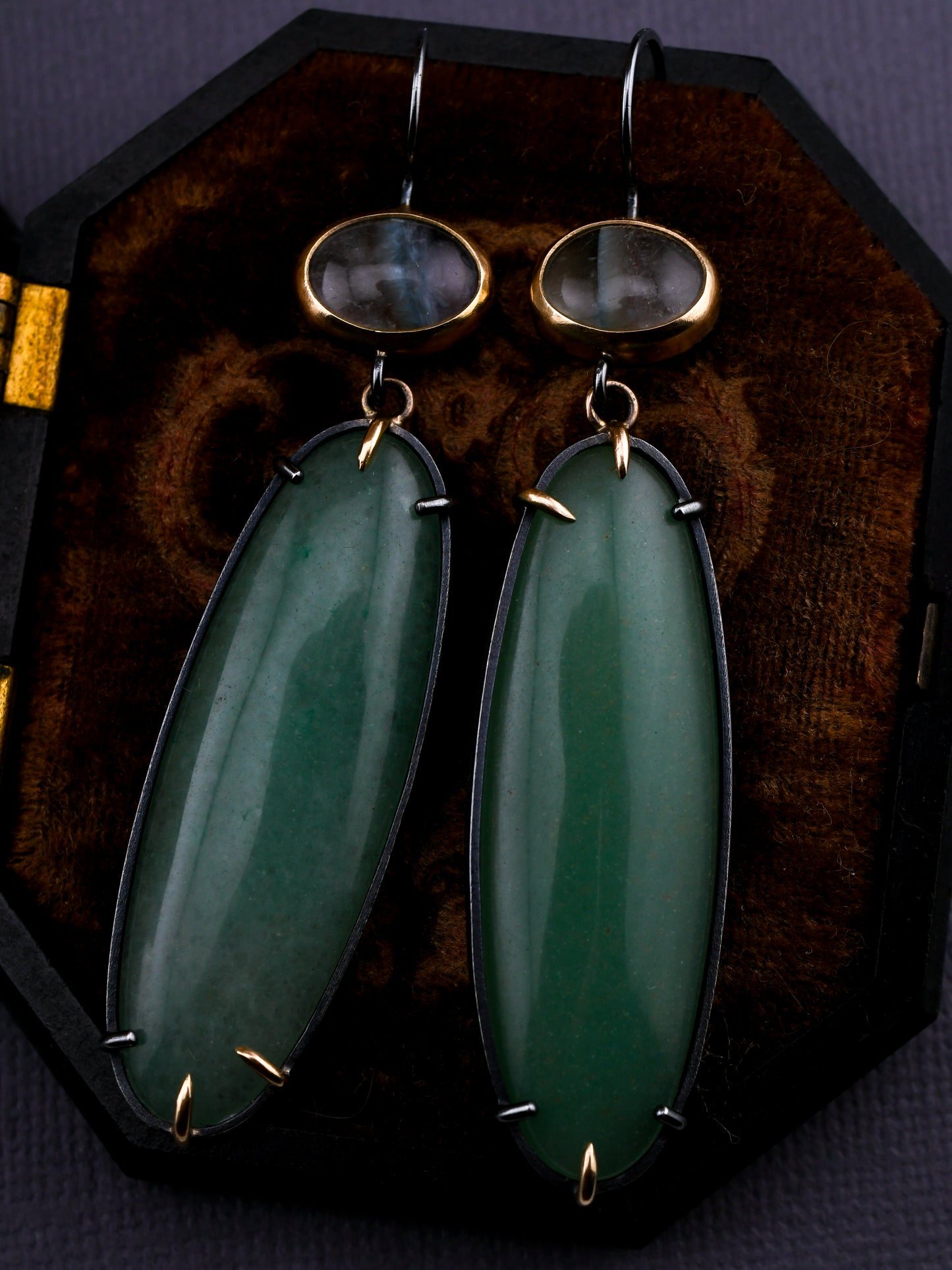 Green stone earrings with gold accents on a dark velvet stand.