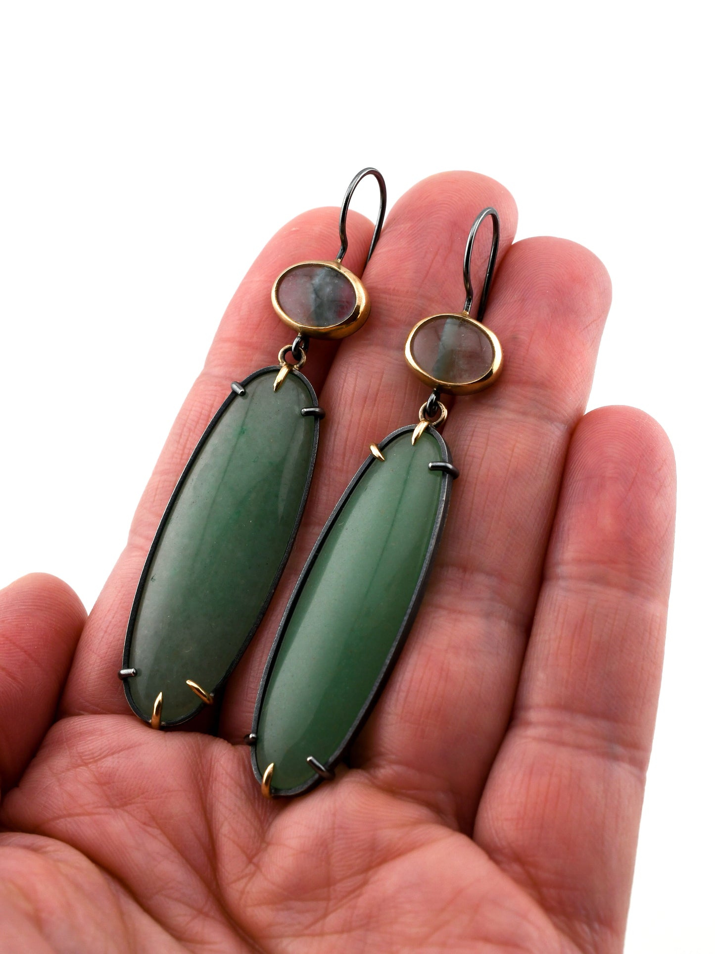 Green earrings held in a hand against a white background