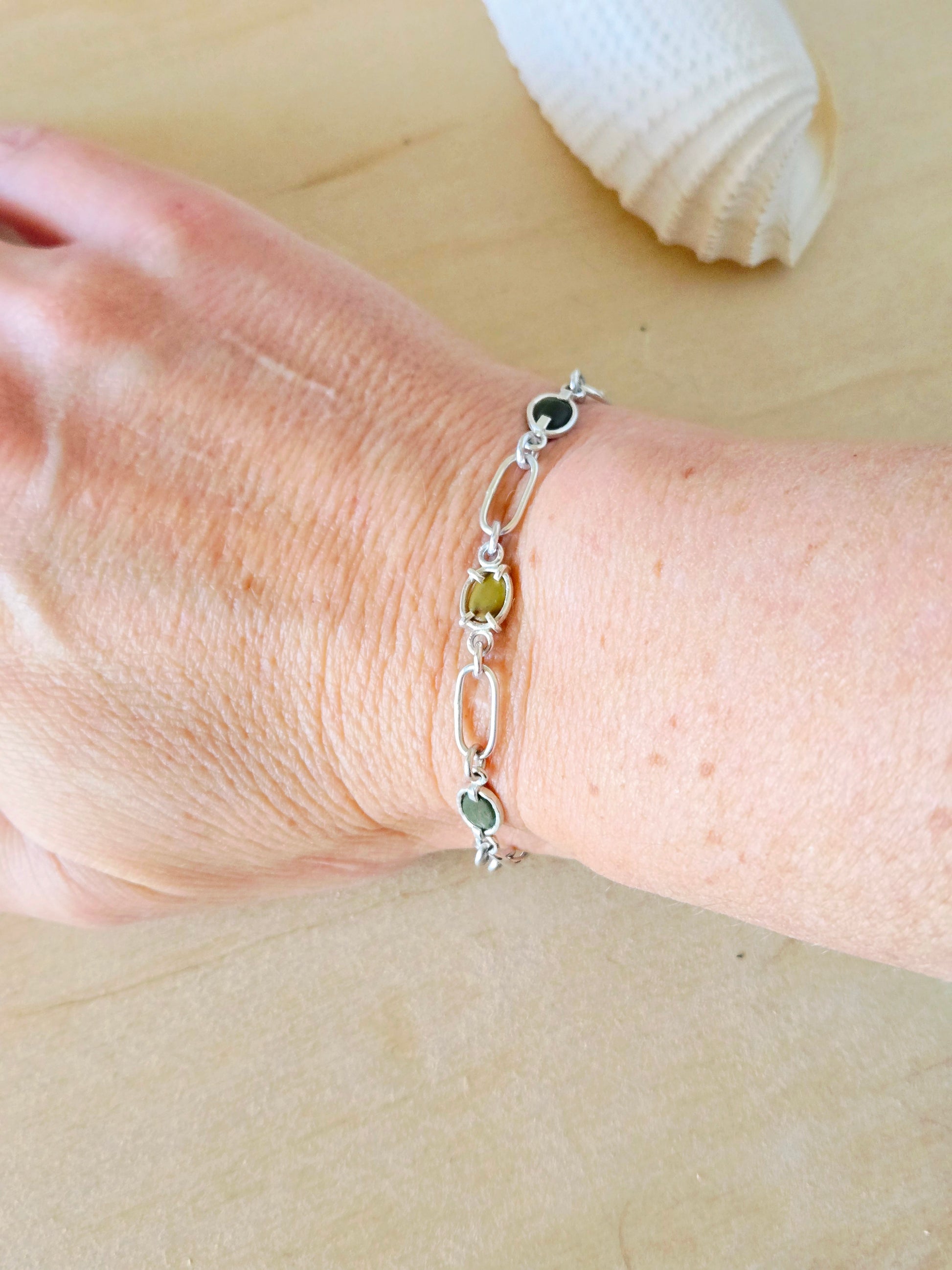 Silver bracelet with green beach stones on a wrist, with a beige background