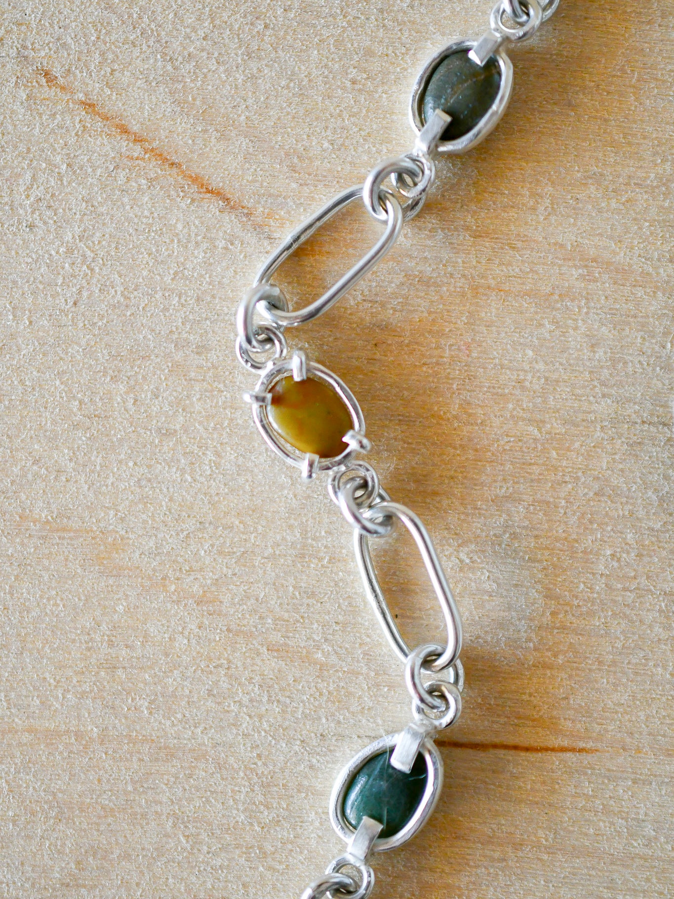 Silver bracelet with green stones on a wooden surface