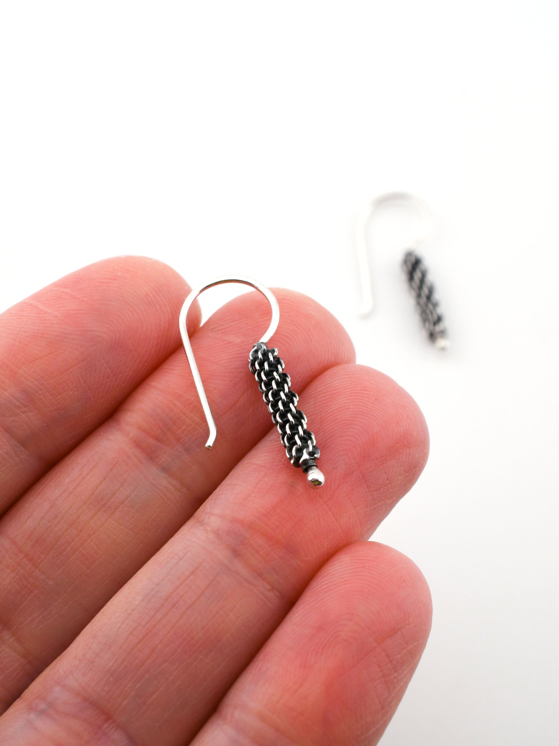 Silver earring with a textured design held between fingers on a white background