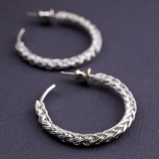 Pair of braided silver hoop earrings on a dark background