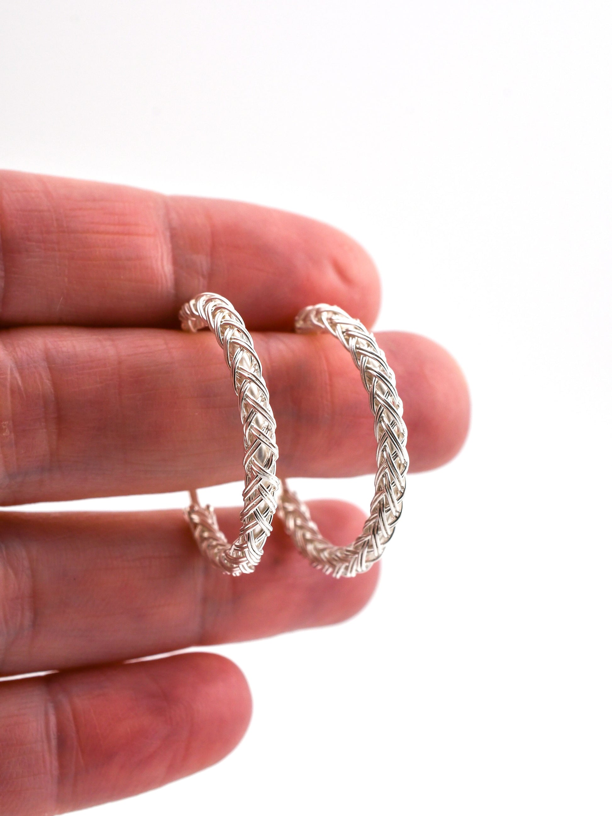 Silver hoop earrings held between fingers on a white background