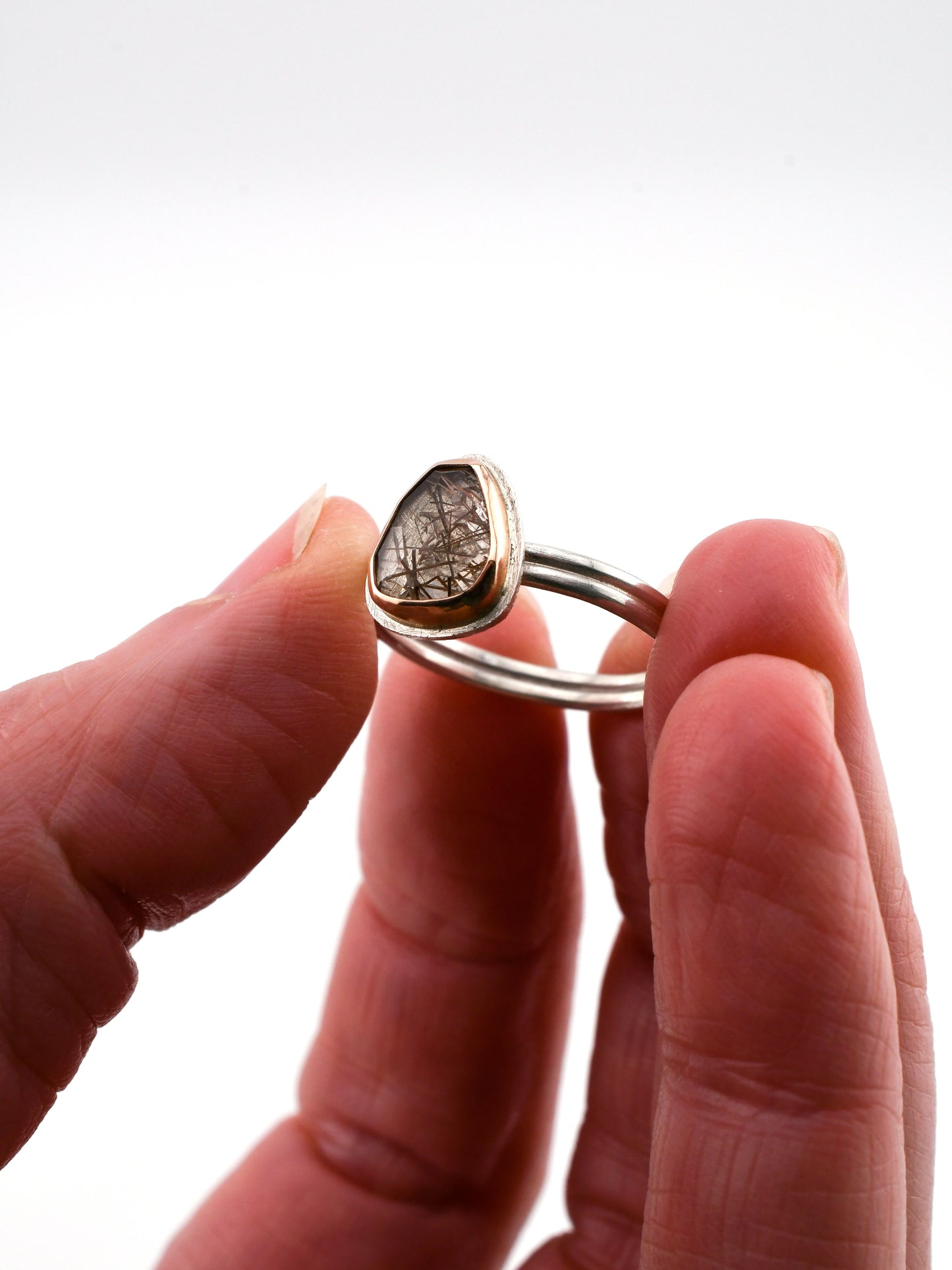 Hand holding a silver ring with a red rutilated quartz gemstone against a white background