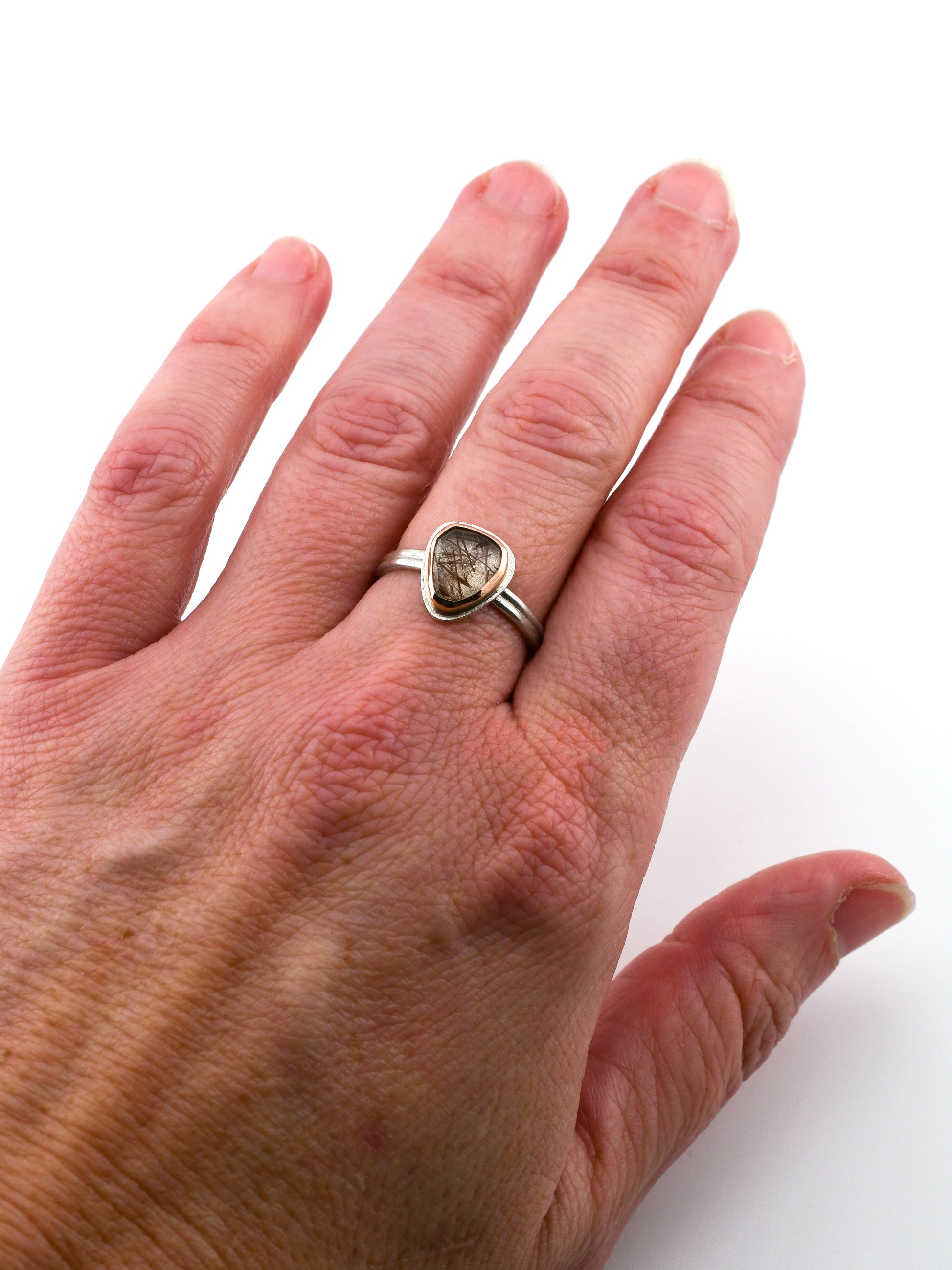 Hand wearing a silver ring with a red rutilated quartz gemstone on a white background