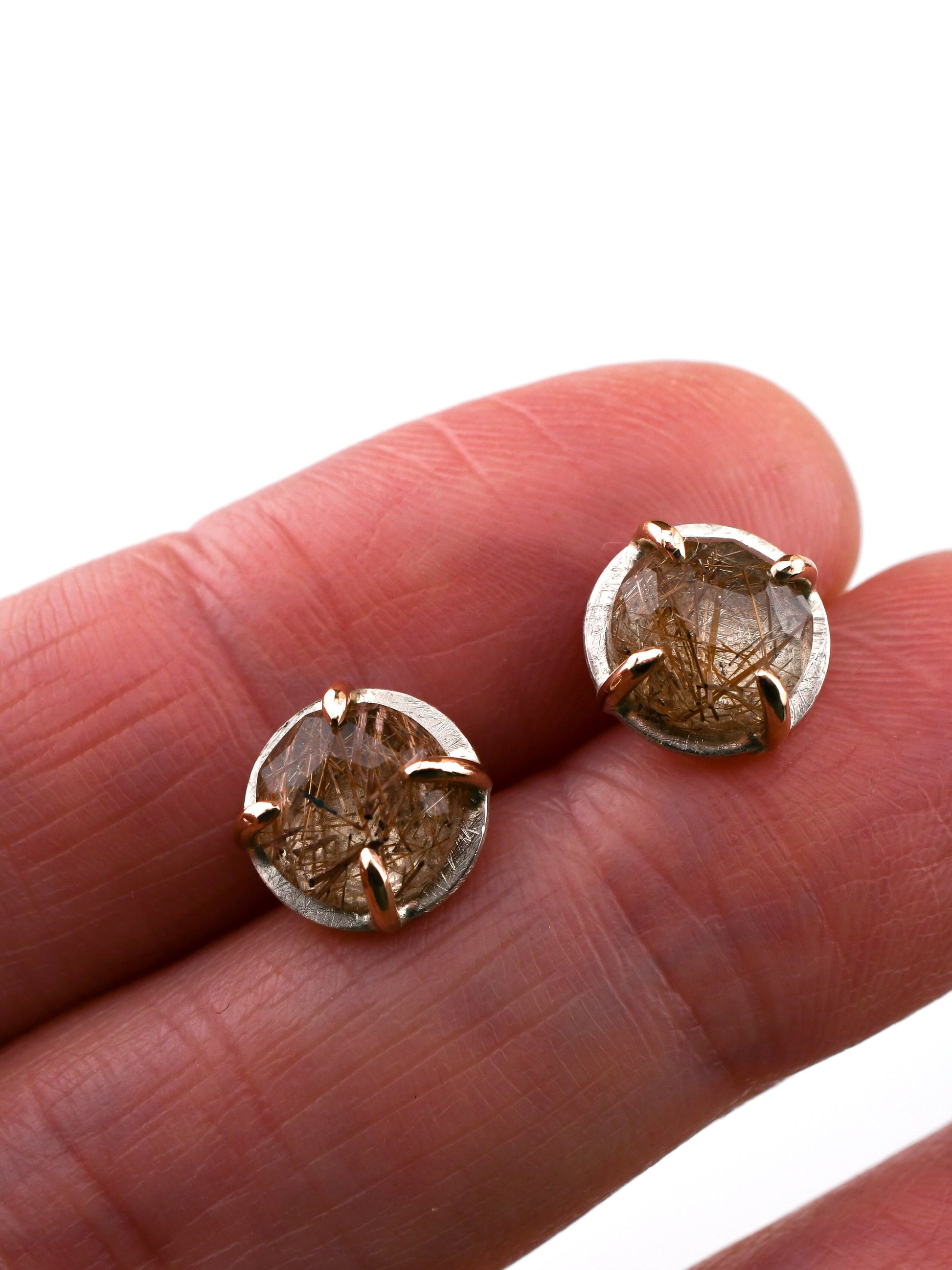 Rose gold and silver gemstone earrings held between fingers on a white background