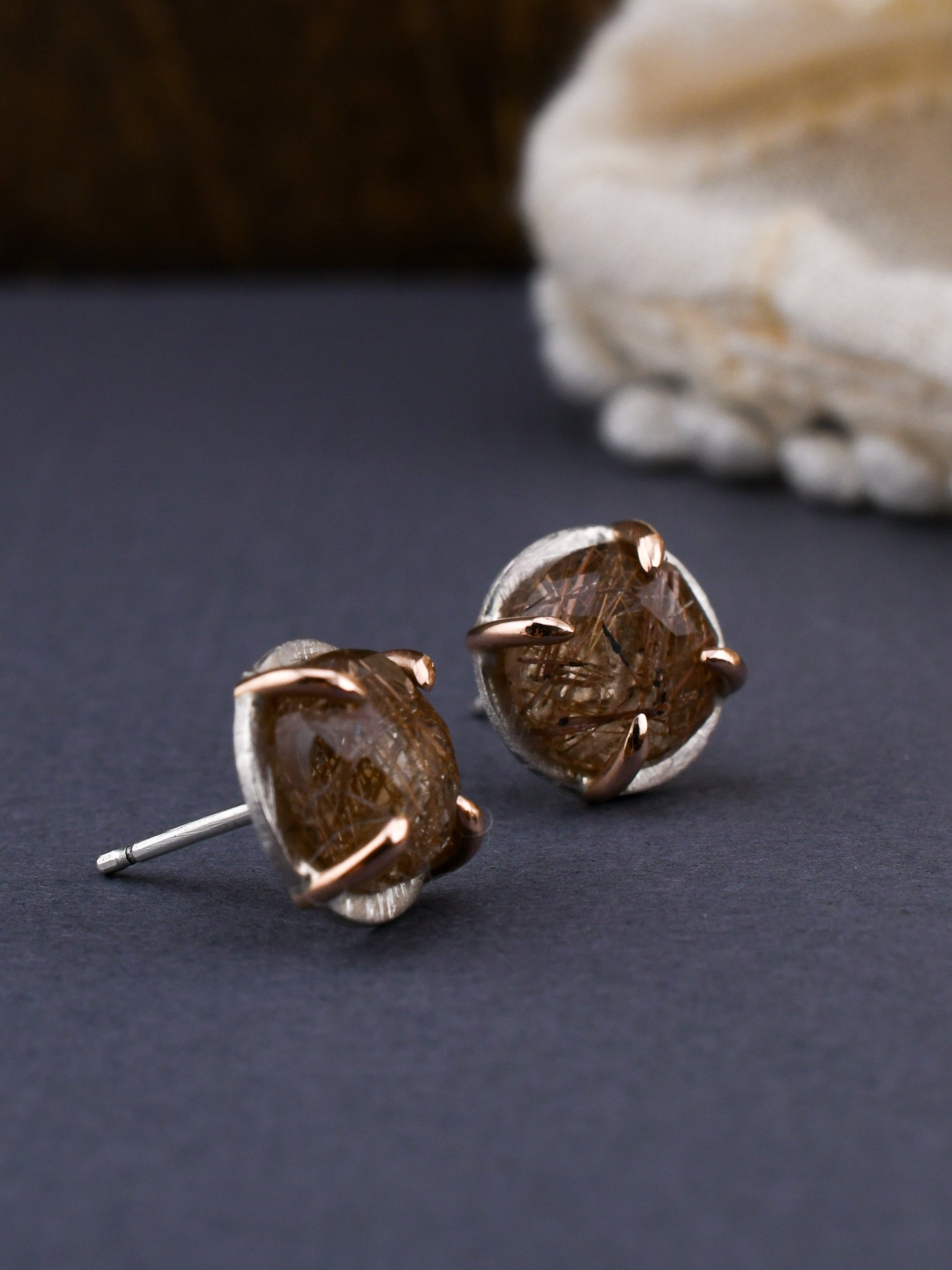 Pair of stud earrings with red rutilated quartz gemstones on a dark surface