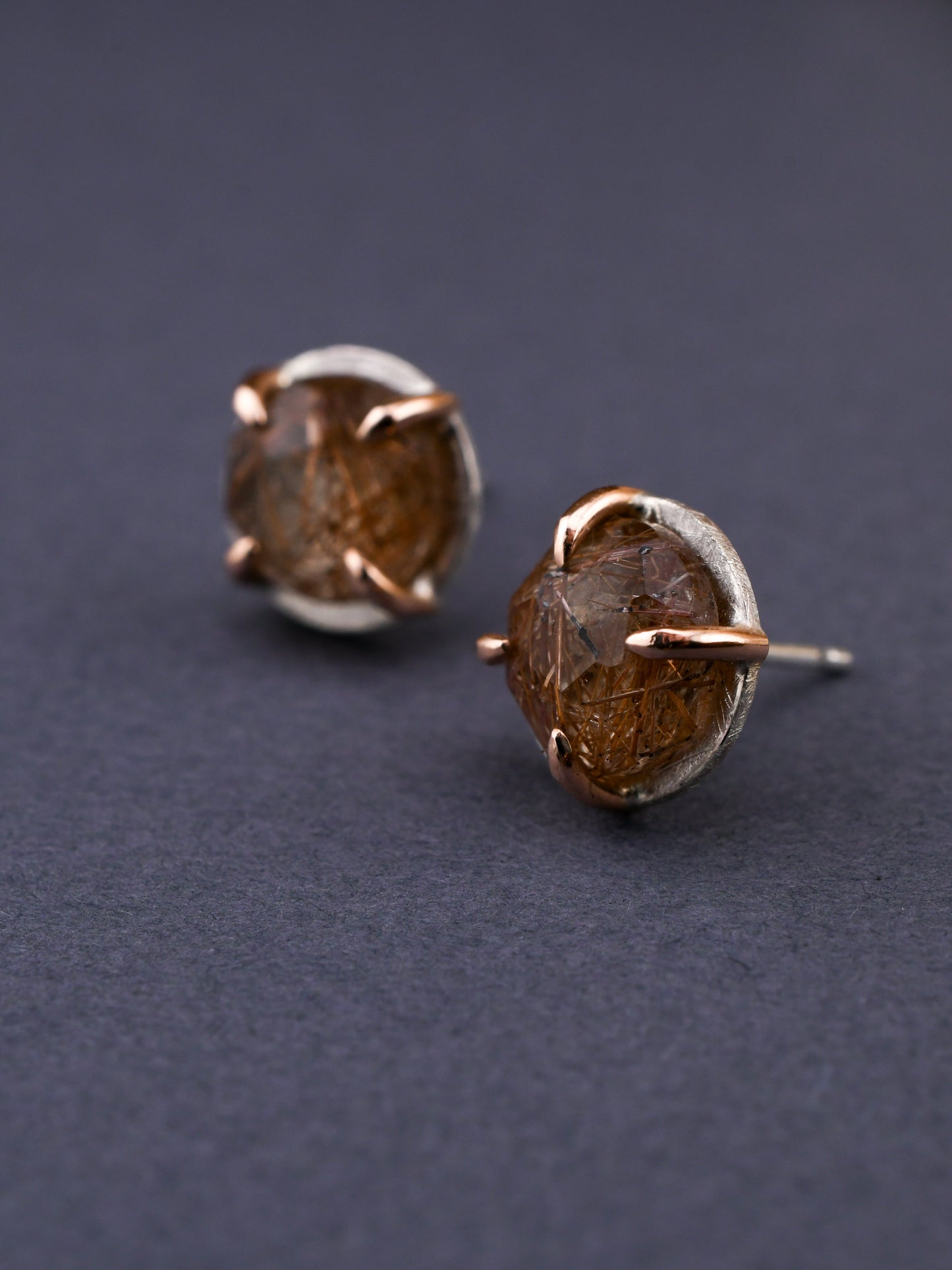 round silver and rose gold stud earrings with red rutilated quartz on a dark gray background