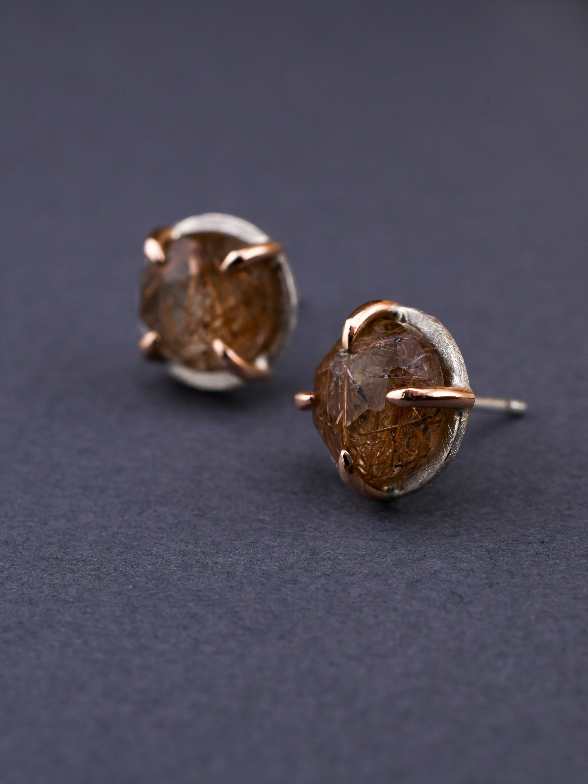 round silver and rose gold stud earrings with red rutilated quartz on a dark gray background