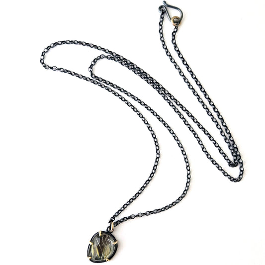 Blackened silver necklace with a rutilated quartz pendant with gold accents on a white background