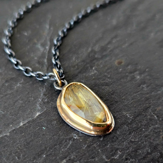 Free form rutilated quartz pendanctwith blackened silver chain on a textured black background