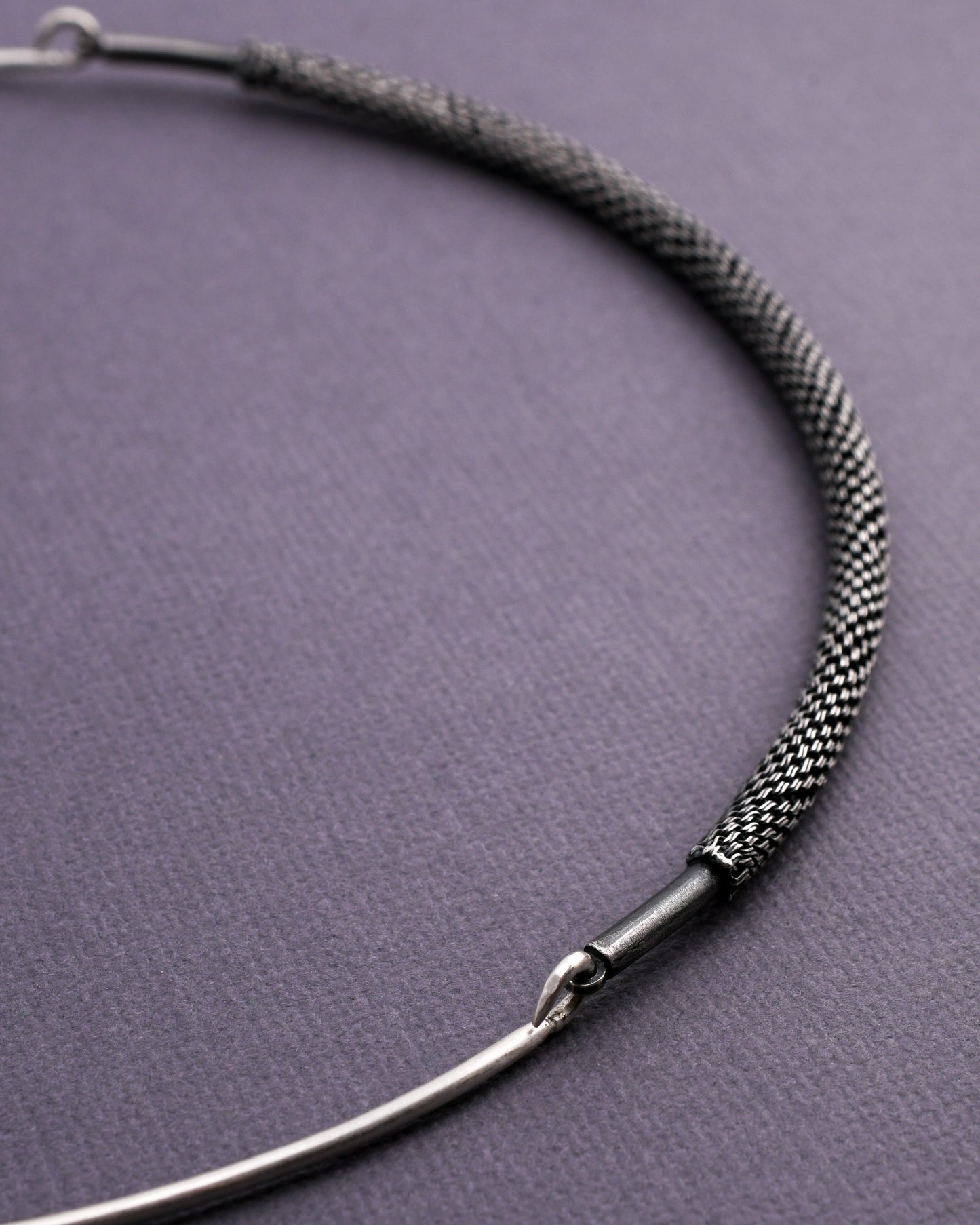 closeup of woven silver necklace on a textured gray background
