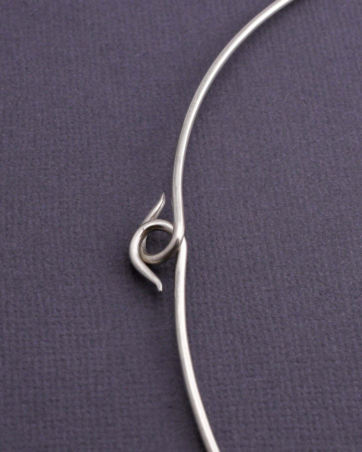 detail of woven silver torque necklace hooked clasp on a dark gray background