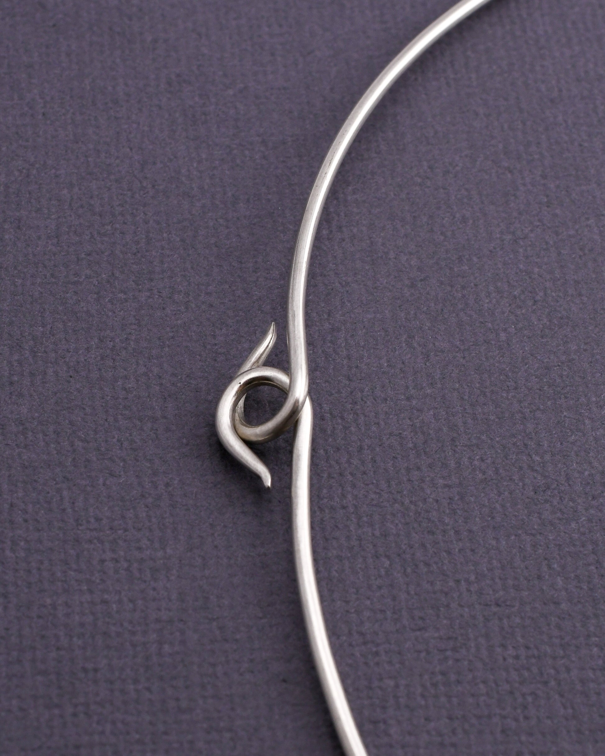 detail of woven silver torque necklace hooked clasp on a dark gray background