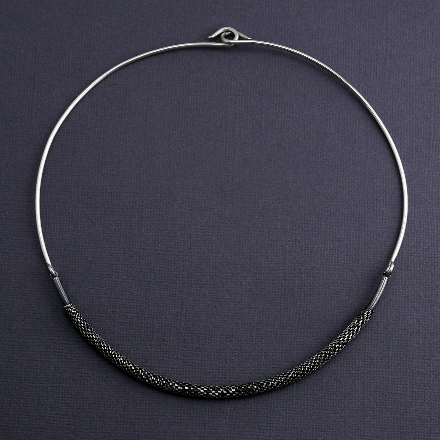 Silver torque necklace with woven element on a dark gray background
