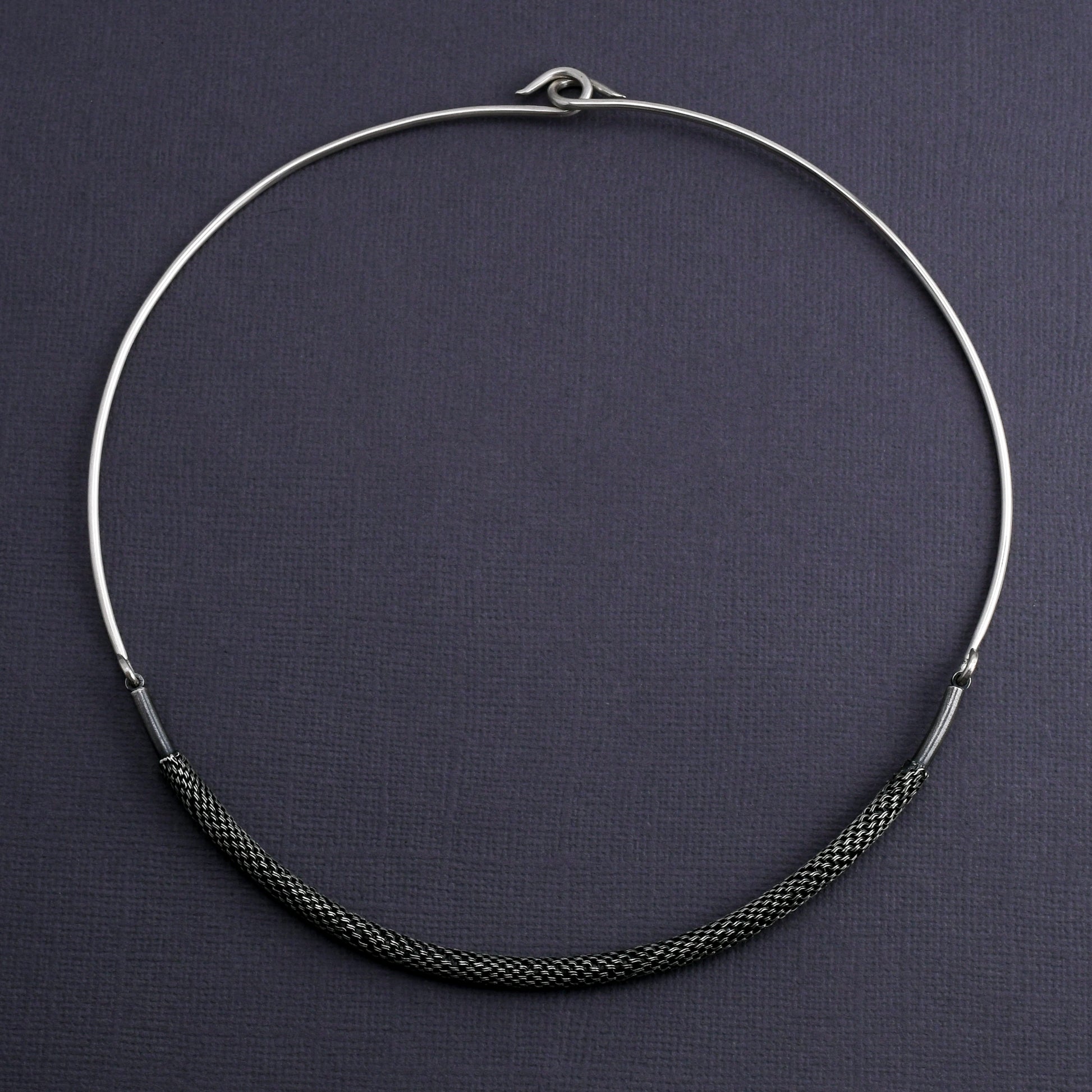 Silver torque necklace with woven element on a dark gray background
