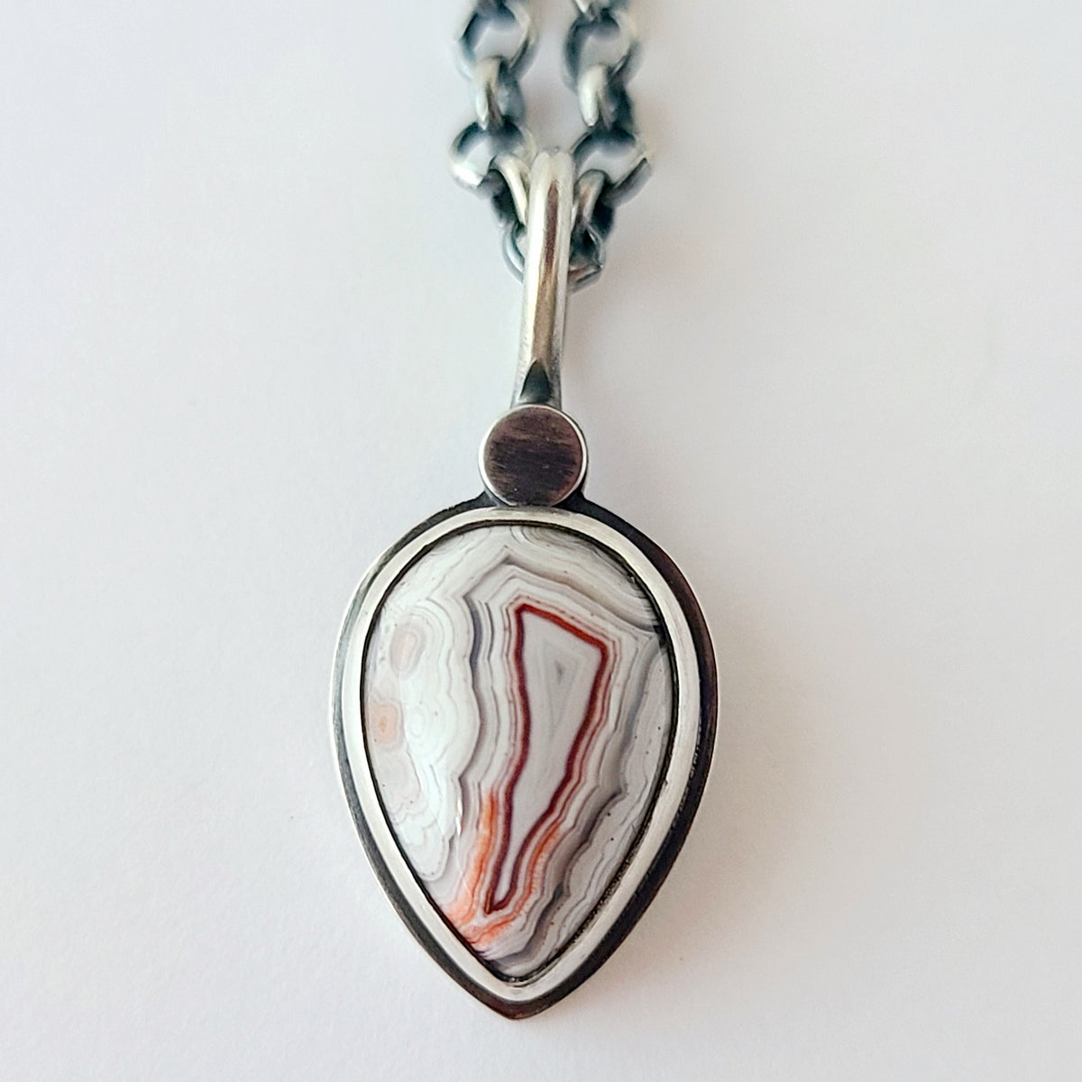 crazy lace teardrop pendant with white red and gray patterns and a silver circle at the top shown on a white background