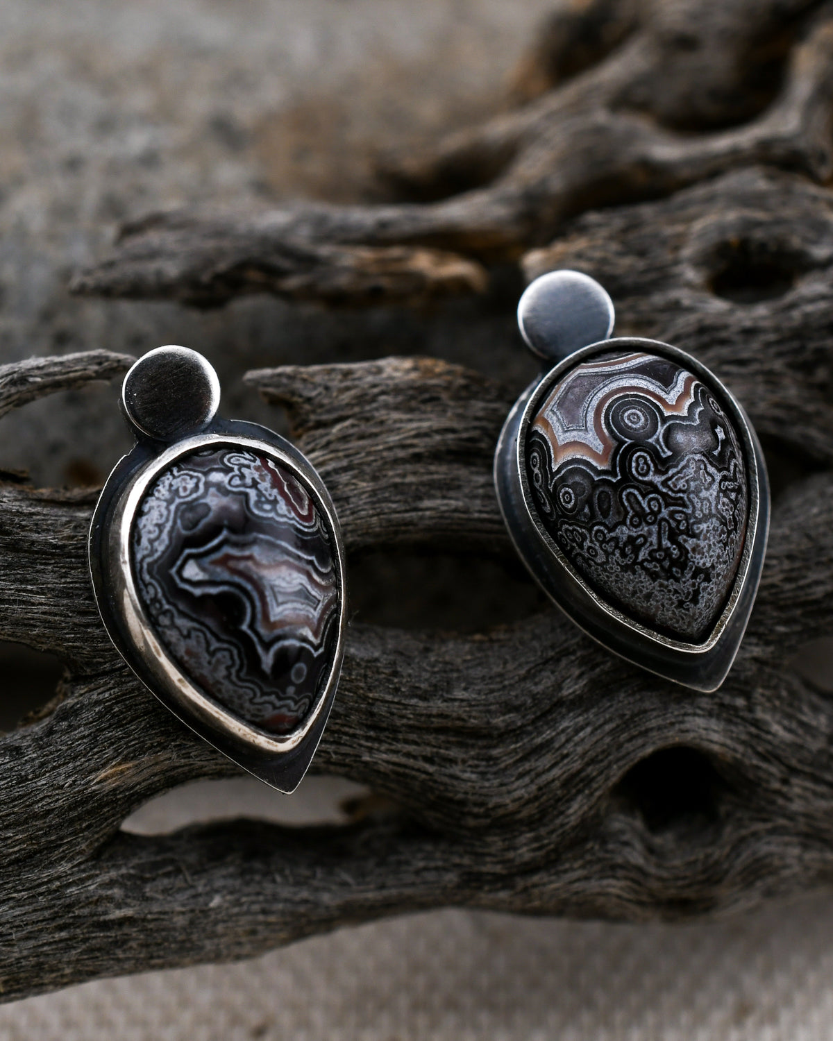 Sterling silver teardrop stud earrings with dark purple and white crazy lace agate displayed on cactus wood