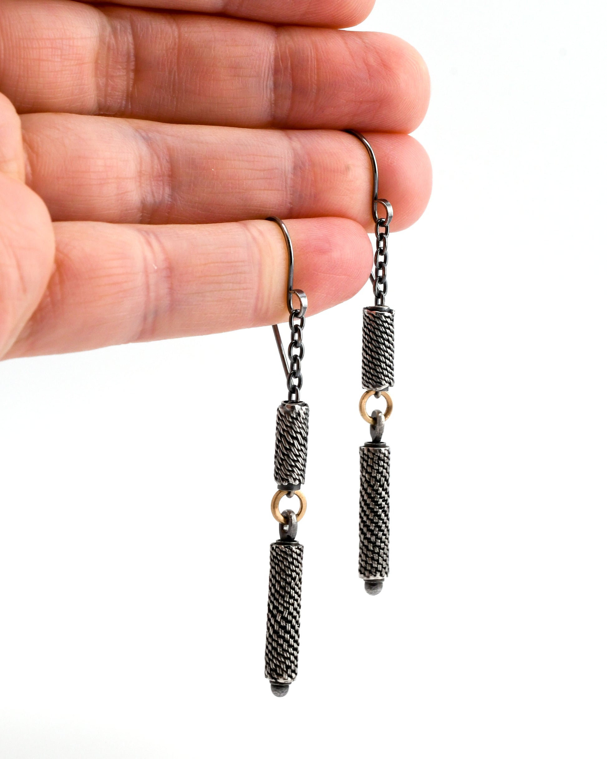 Woven silver bead and chain earrings with 14k gold links held in a hand over a white background