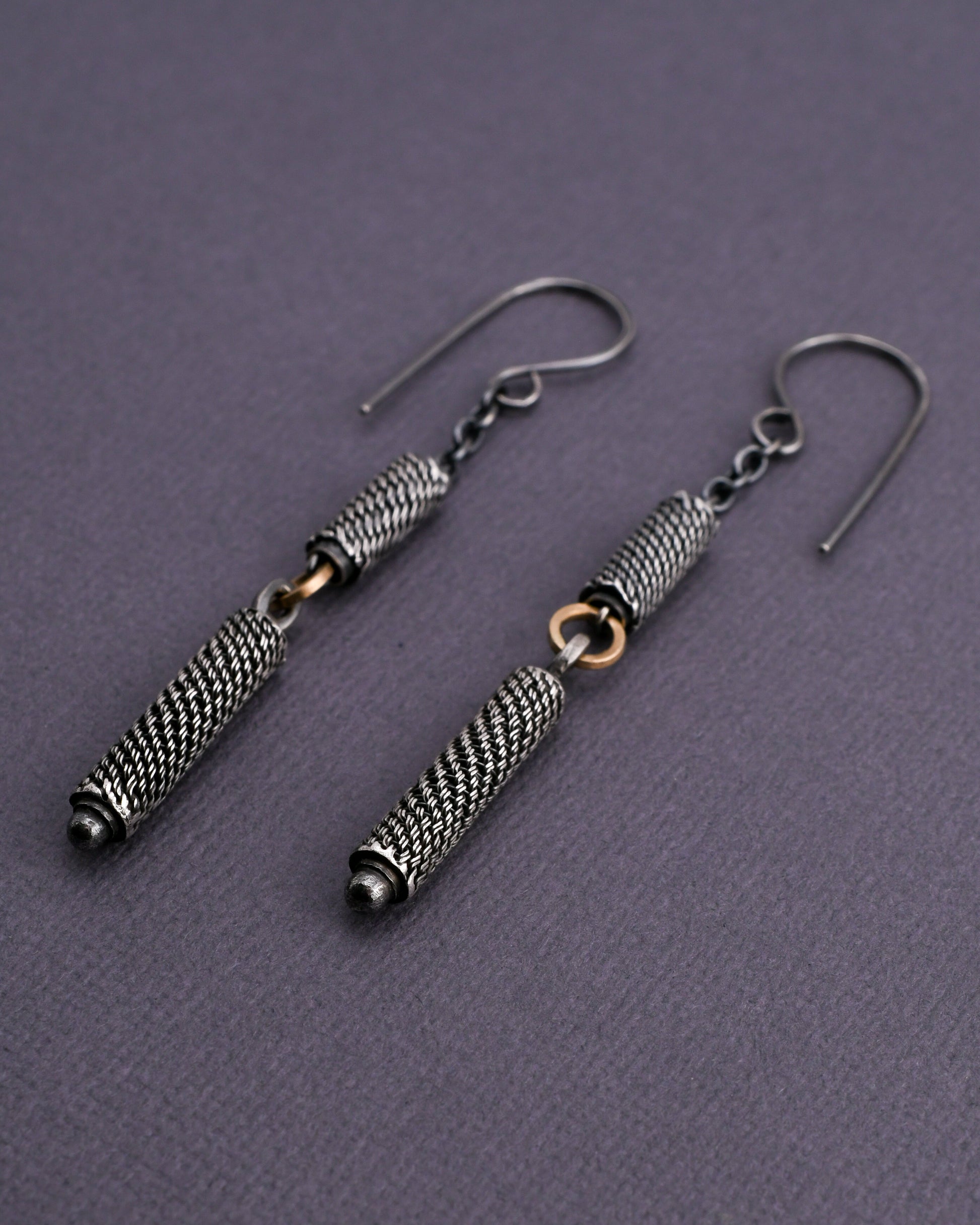 Pair of silver earrings with woven beads and 14k gold links on a textured gray background
