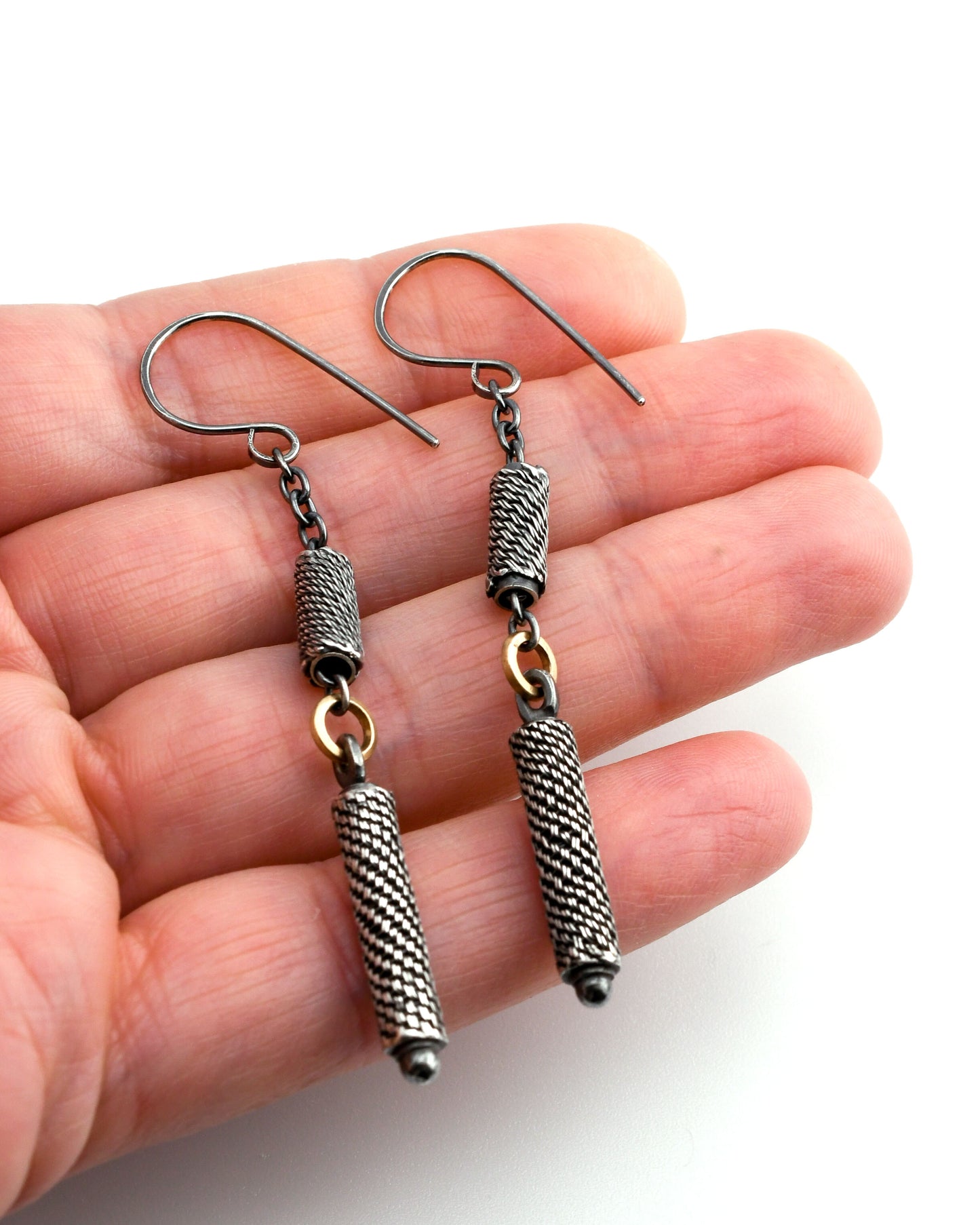 Silver earrings with woven beads and gold links held in a hand against a white background