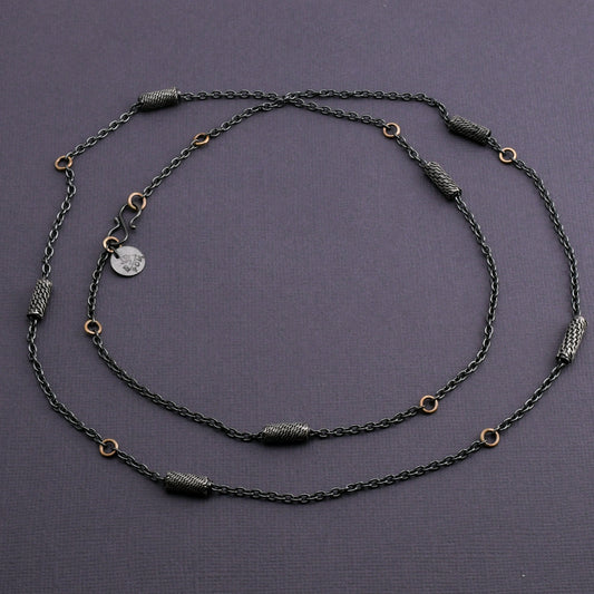 Black silver chain necklace with woven silver beads and 14k gold links on a dark gray background