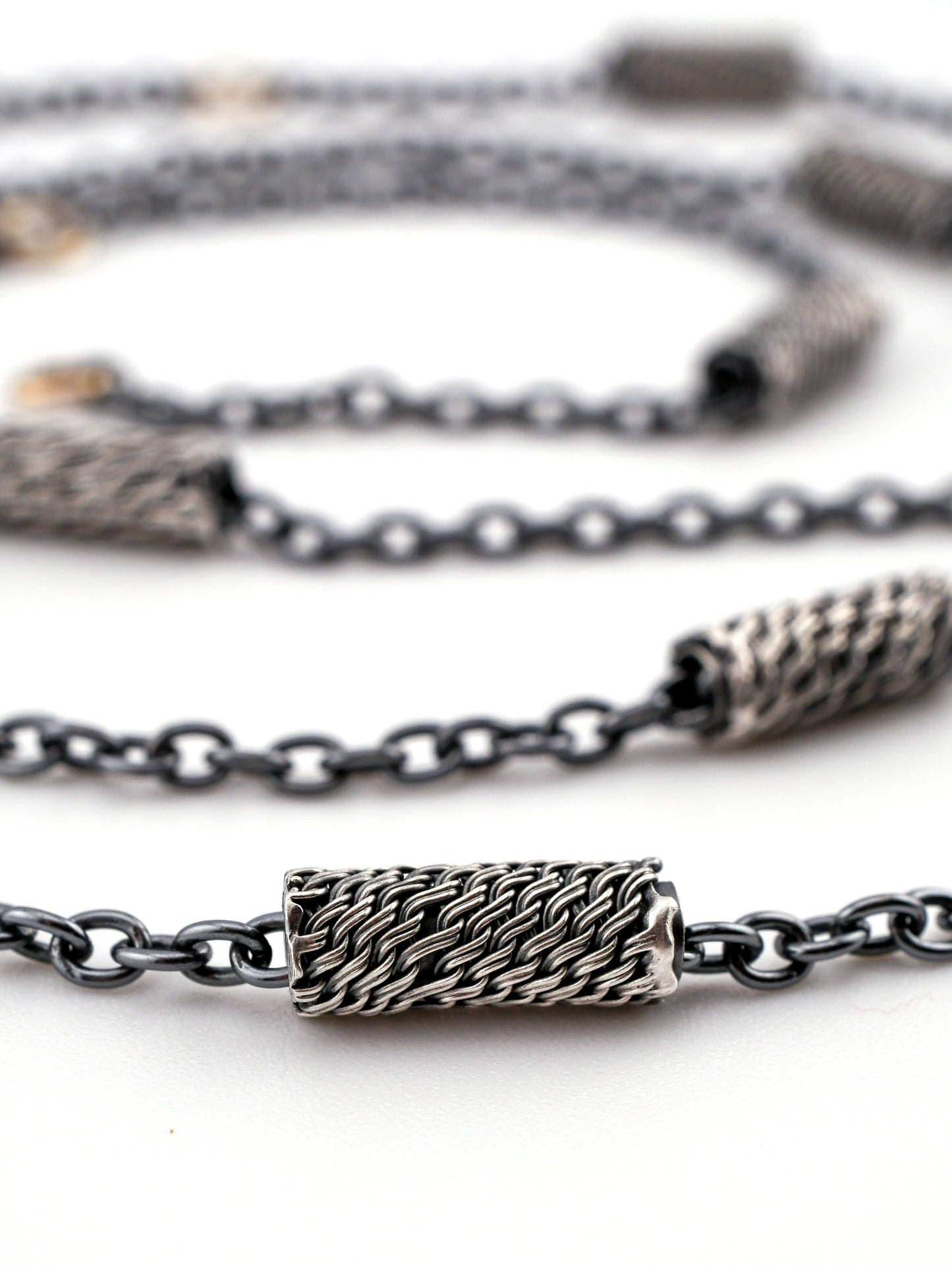 Close-up of a silver chain necklace with woven silver beads on a white background