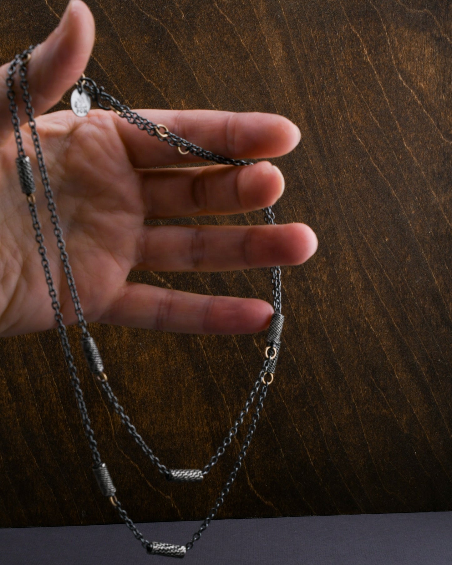 Hand holding a chain necklace against a wooden background