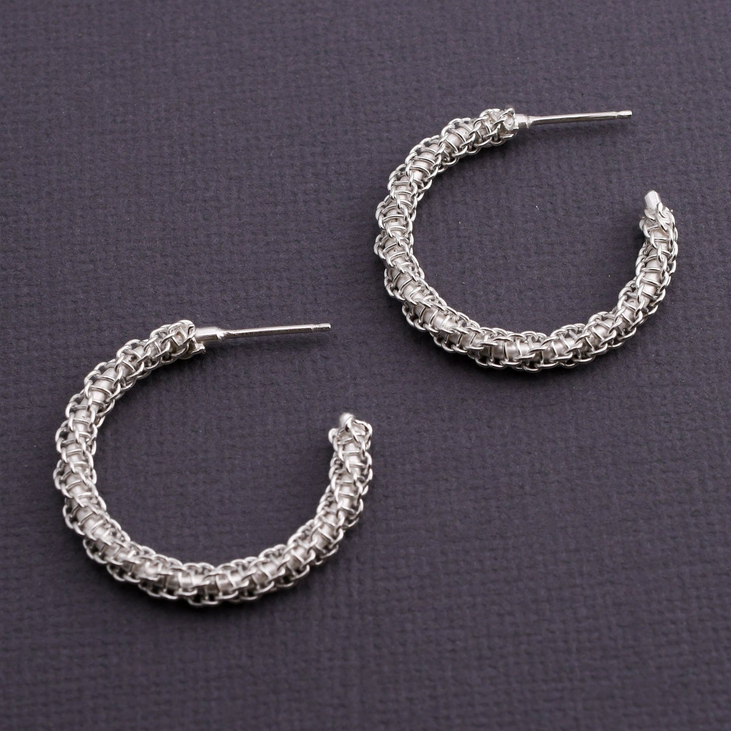 Pair of woven silver hoop earrings on a dark gray background