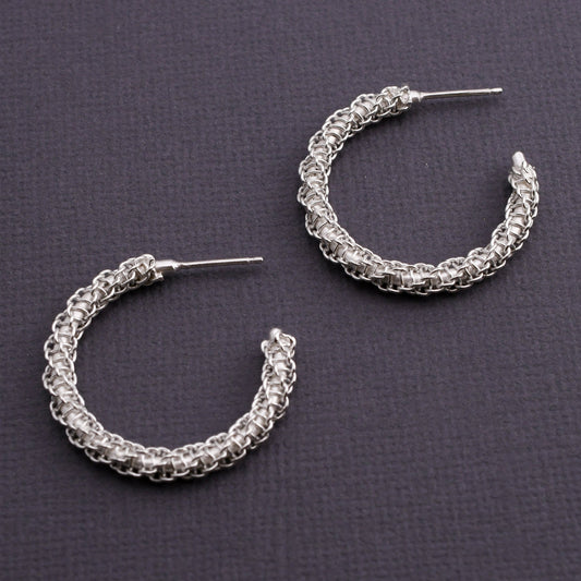 Pair of woven silver hoop earrings on a dark gray background