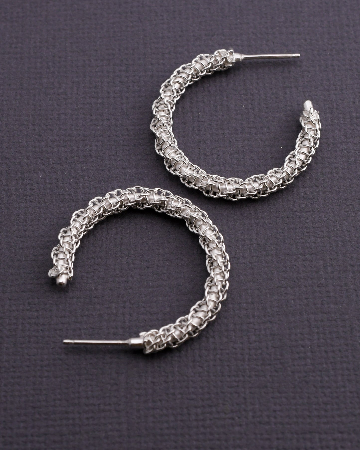 Pair of woven silver hoop earrings on a dark gray background