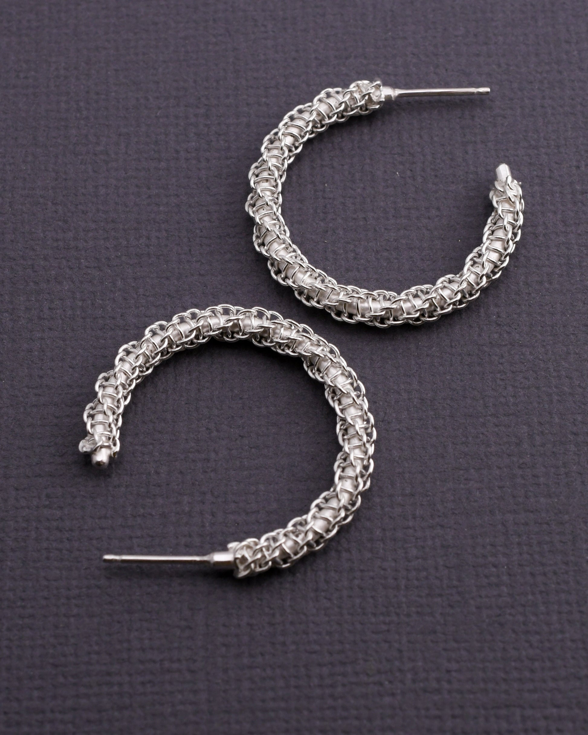 Pair of woven silver hoop earrings on a dark gray background