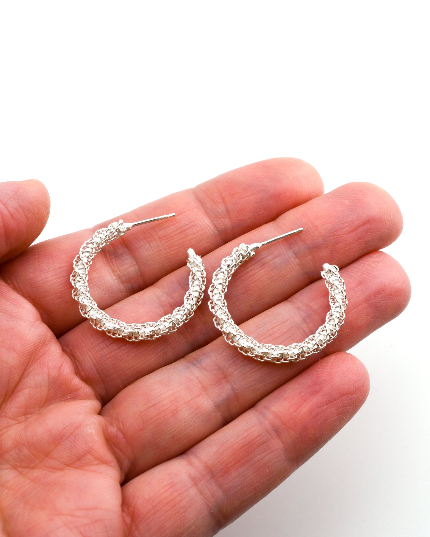 Woven silver hoop earrings held in a hand against a white background