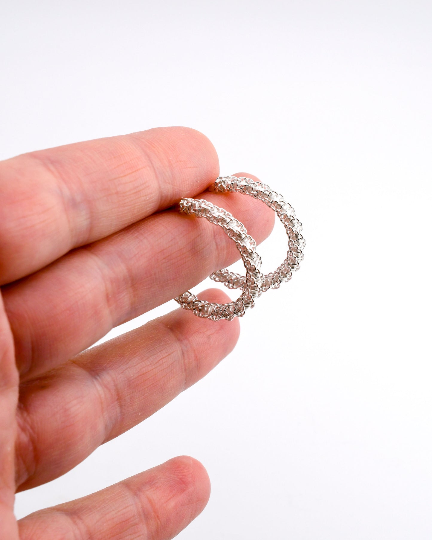 Hand holding a woven silver hoop earring against a white background