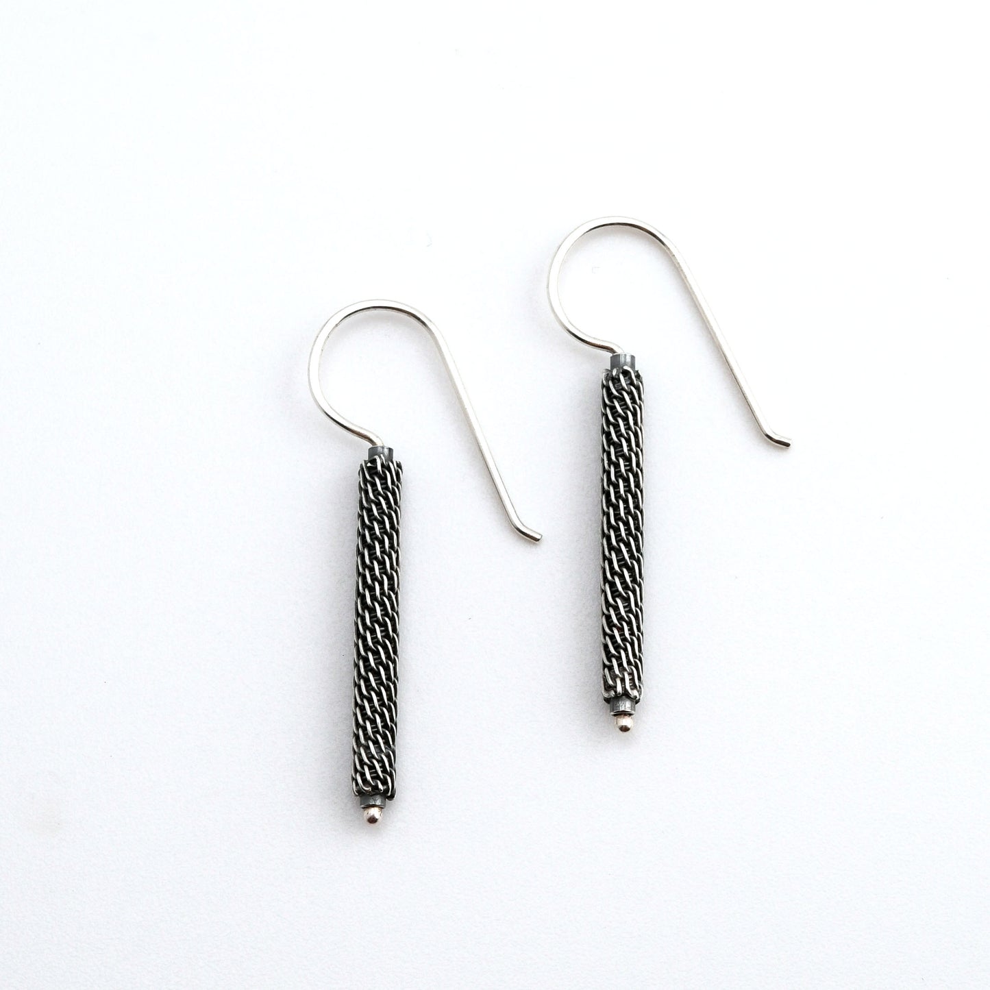Pair of  oxidized woven silver column earrings on a white background