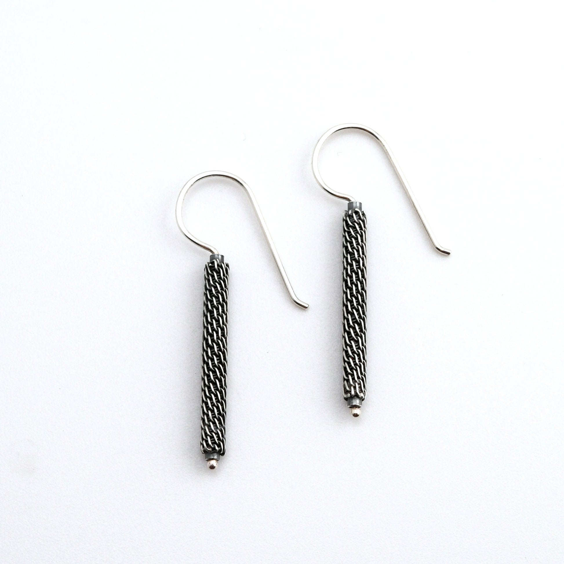 Pair of  oxidized woven silver column earrings on a white background