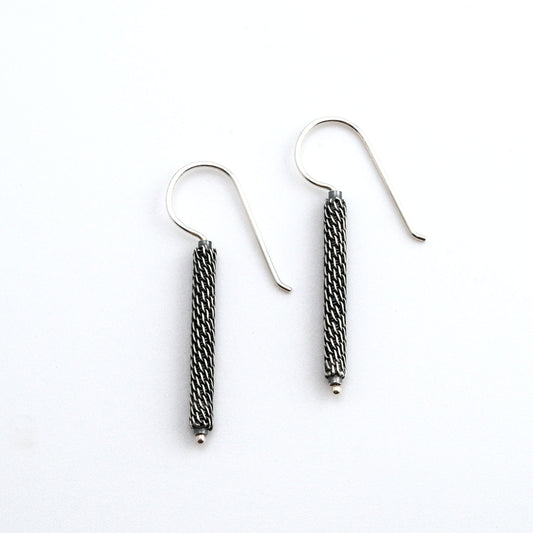 Pair of  oxidized woven silver column earrings on a white background