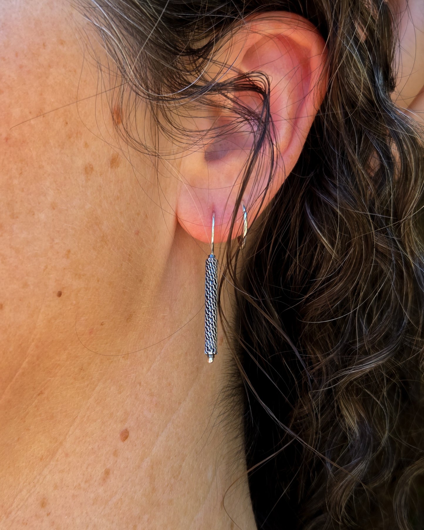 Close-up of oxidized woven silver column earring worn on a person