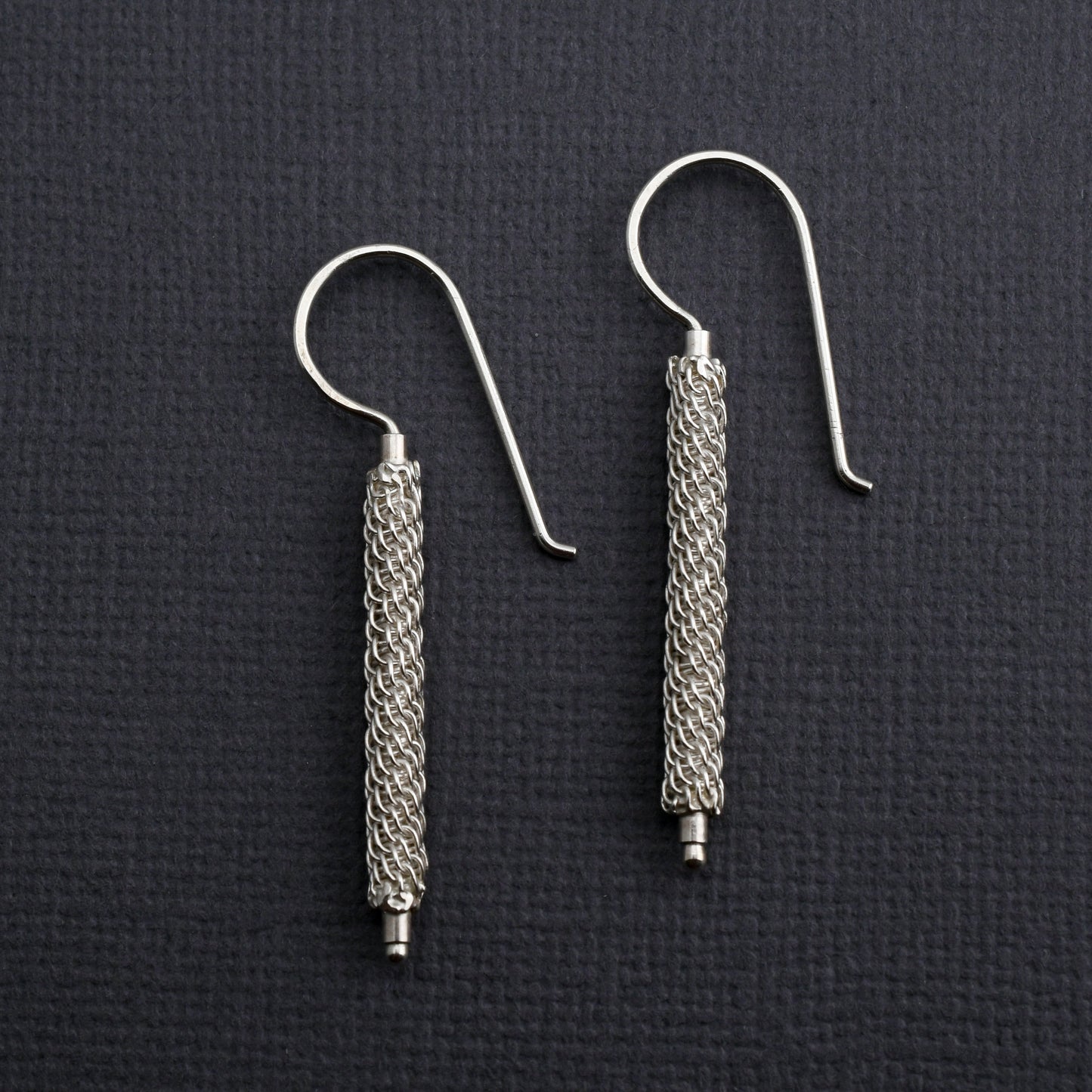 Pair of woven silver column earrings on a dark textured background