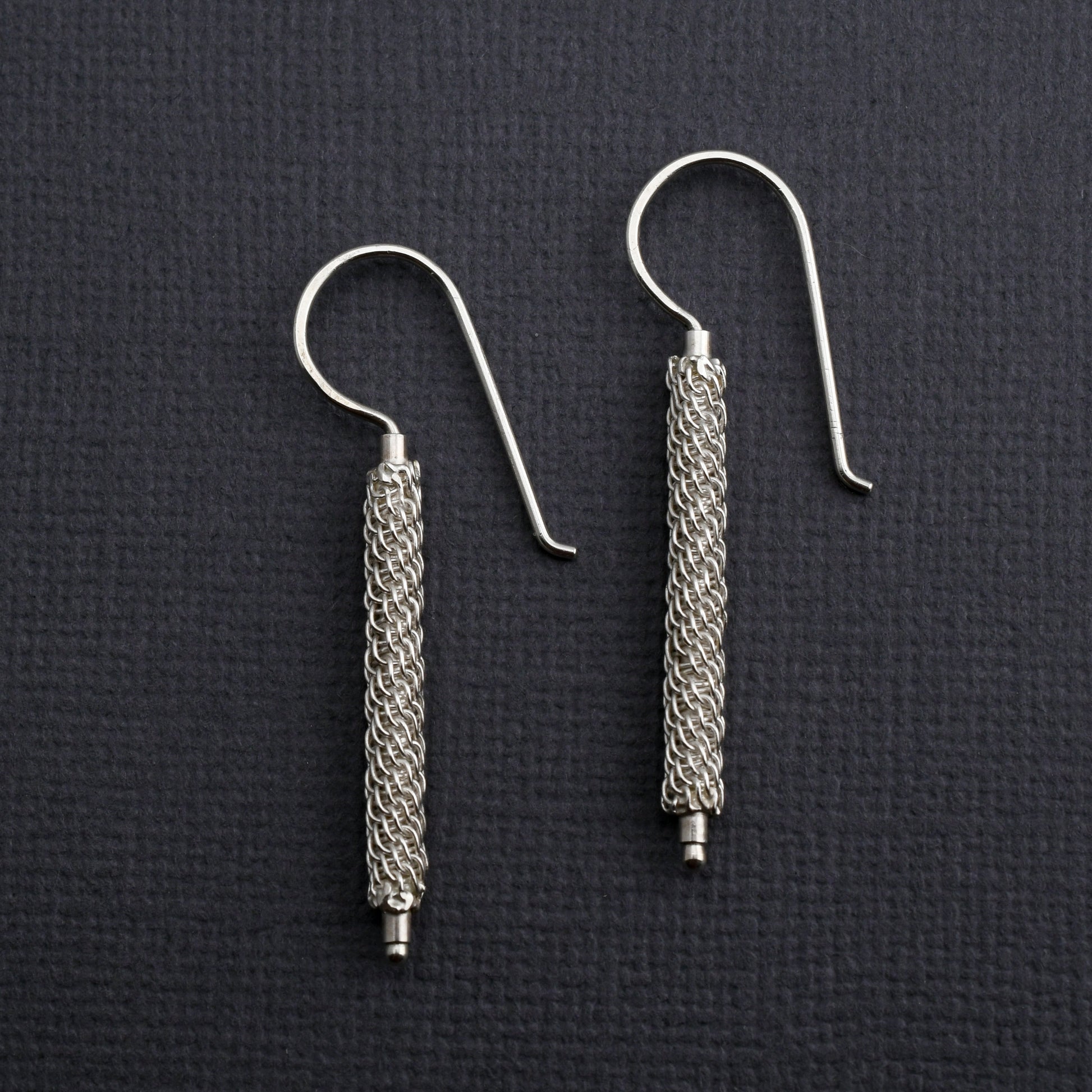 Pair of woven silver column earrings on a dark textured background