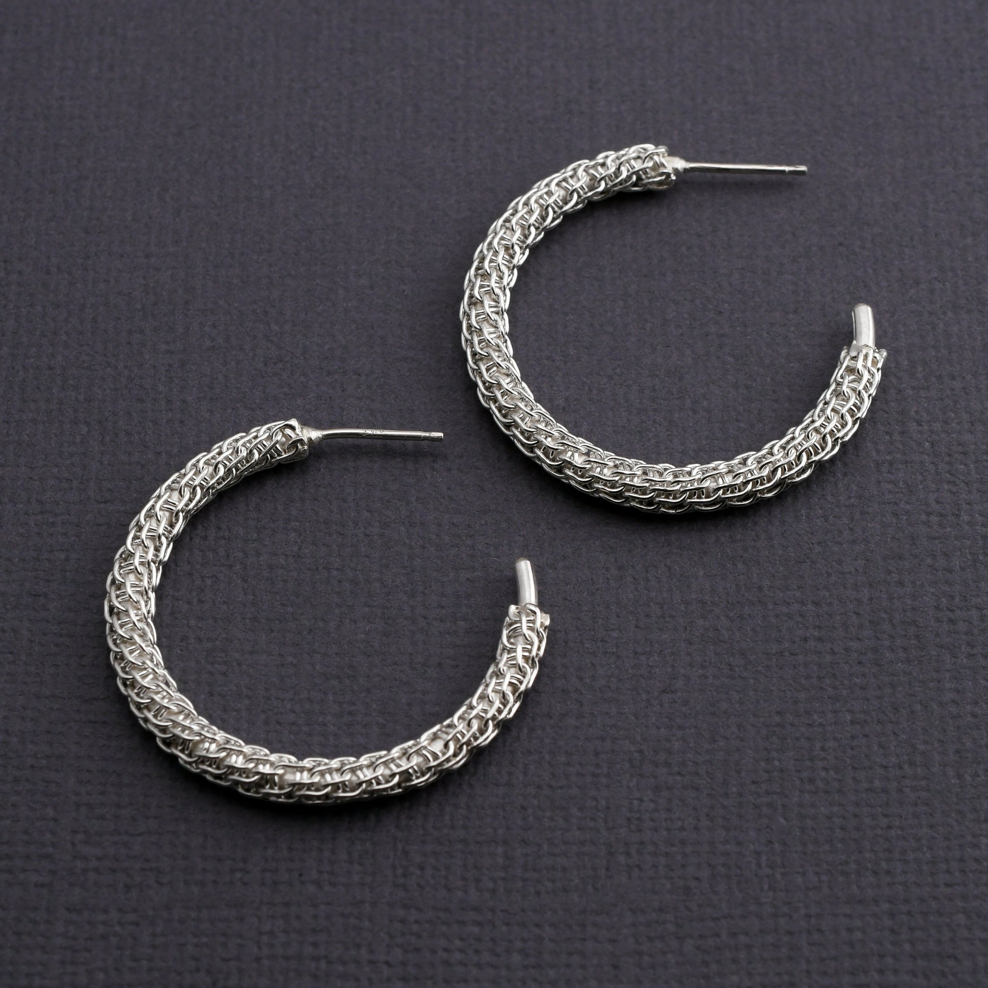 Pair of woven silver hoop earrings on a dark gray background