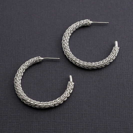 Pair of woven silver hoop earrings on a dark gray background