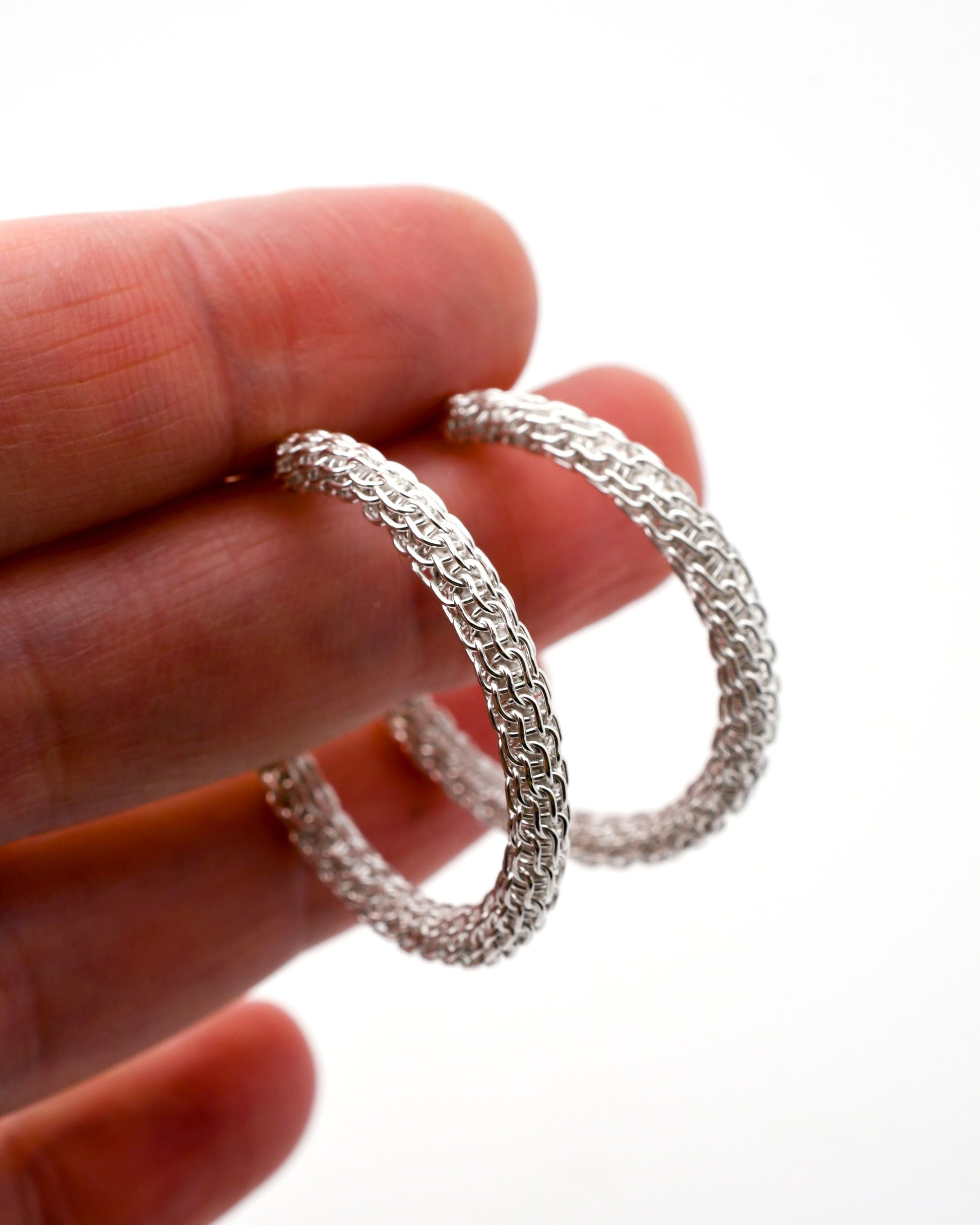 Spiral woven silver hoop earrings held between fingers against a white background