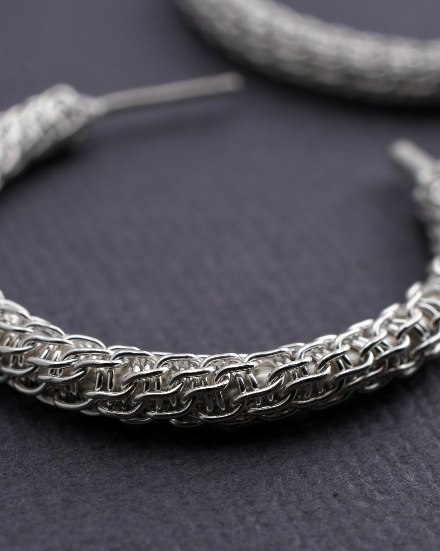 Close-up of a spiral woven silver hoop earring on a dark surface