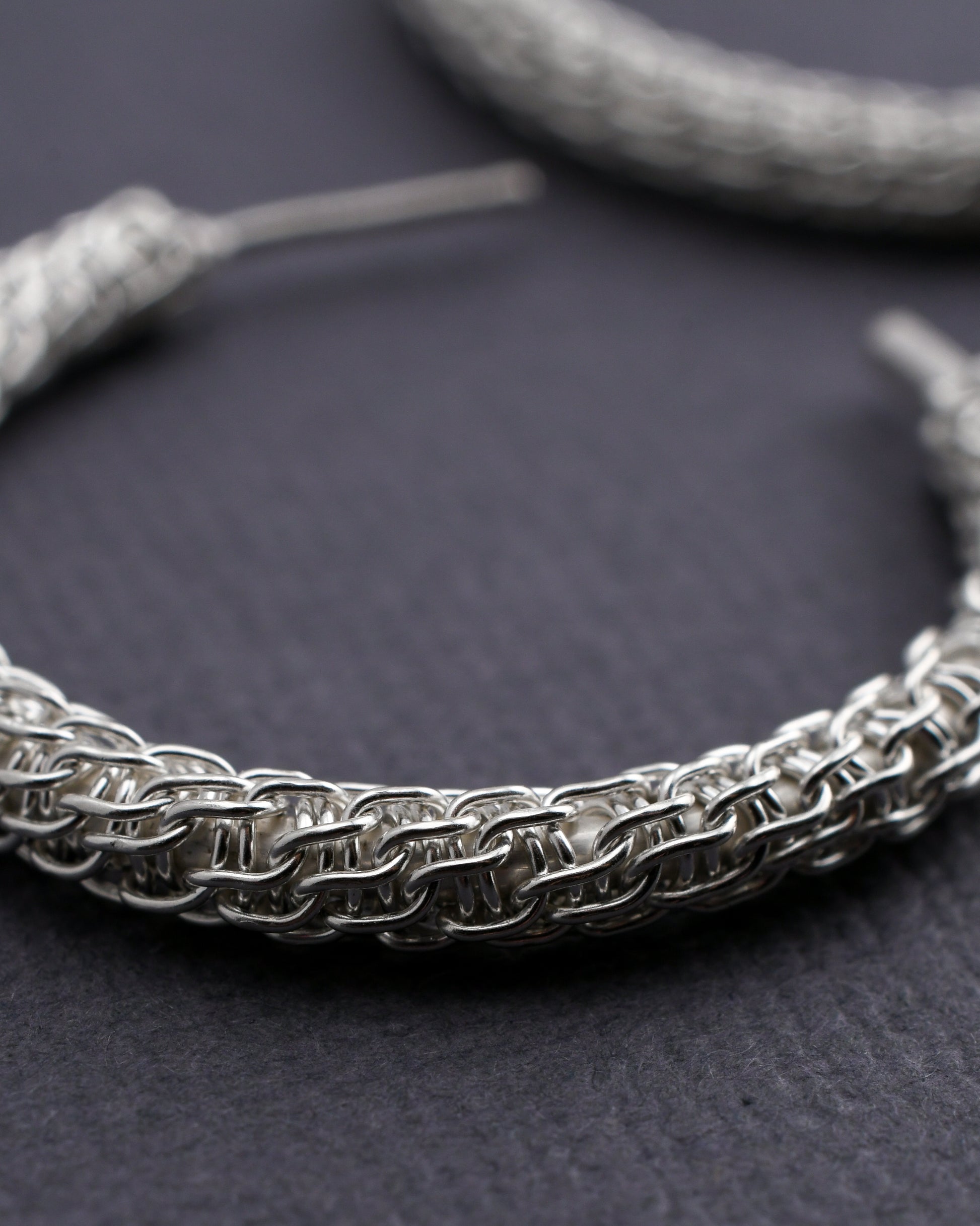 Close-up of a spiral woven silver hoop earring on a dark surface