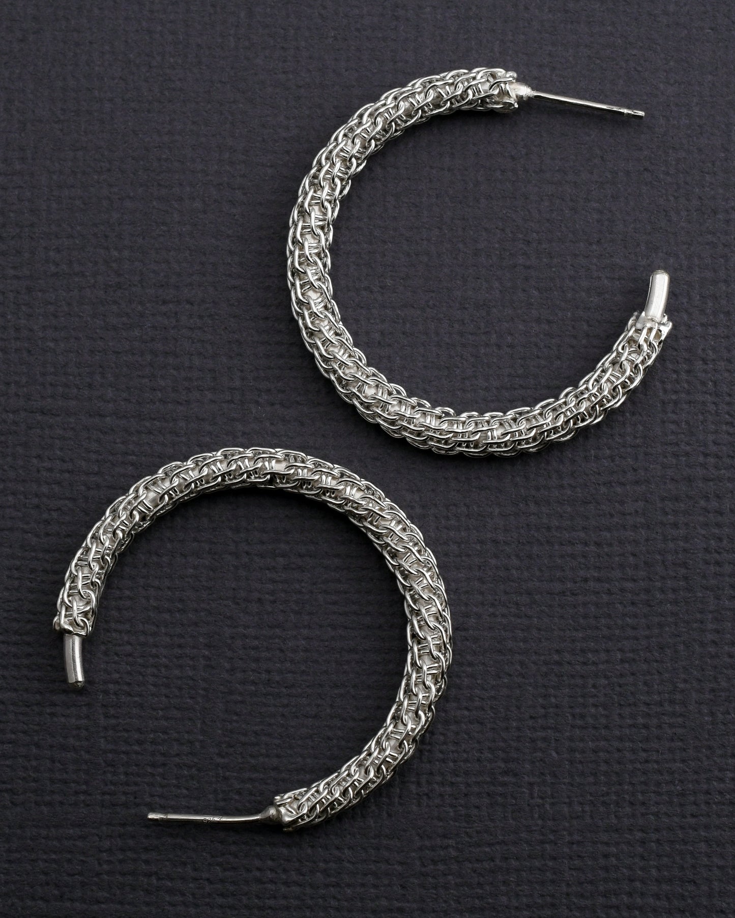 woven silver hoop earrings on a textured gray surface