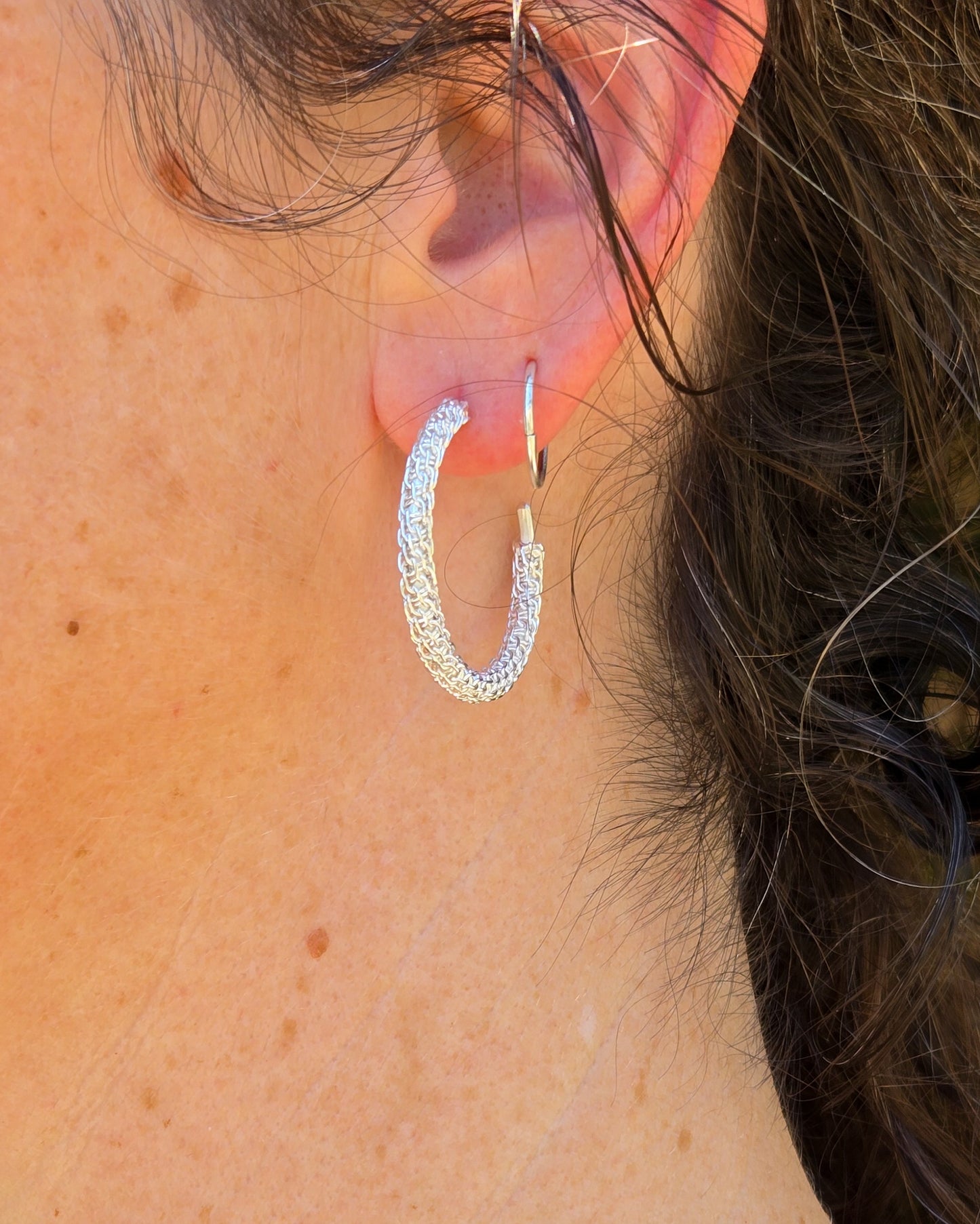 Close-up of a person wearing a silver hoop earring.