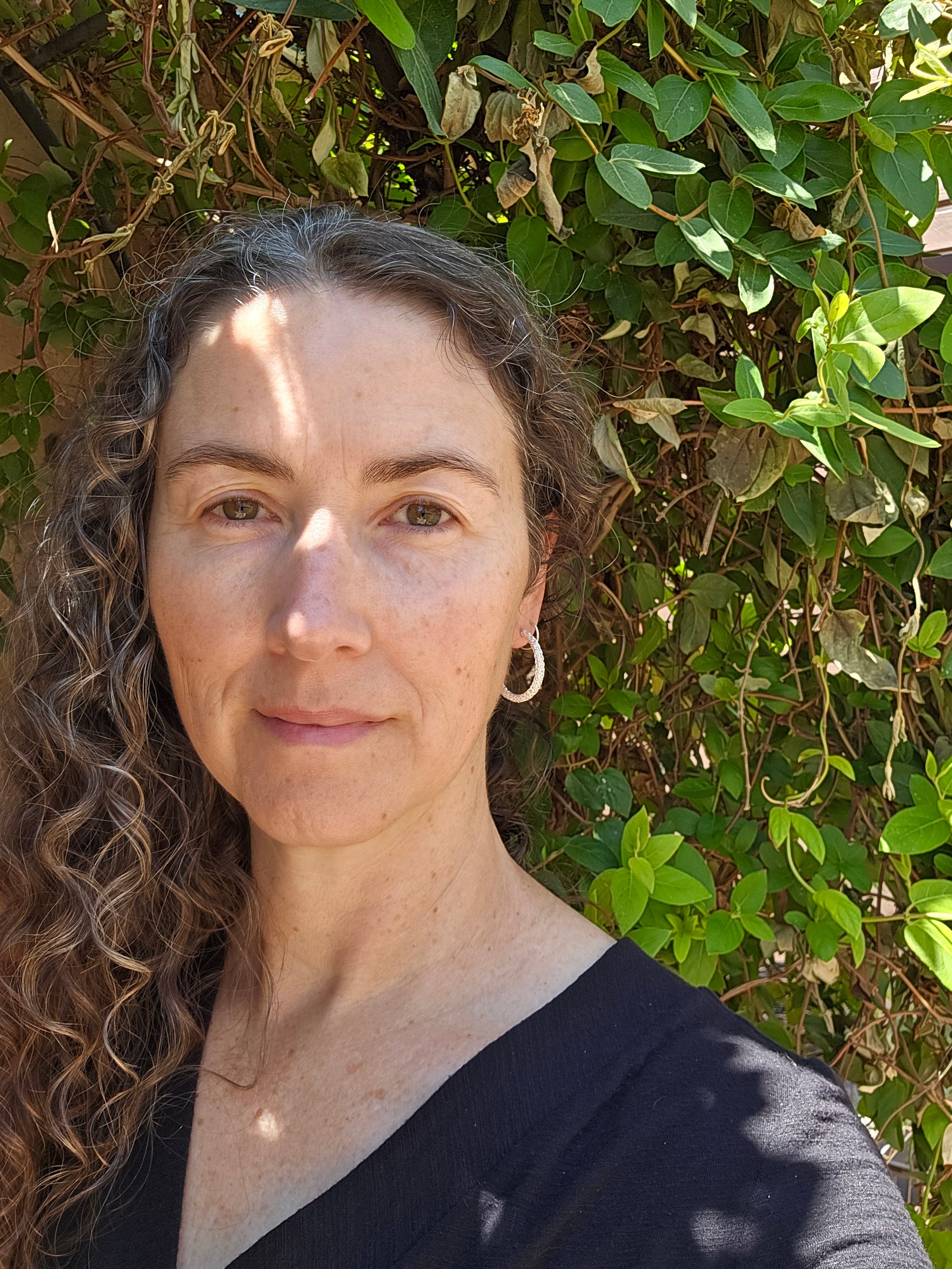 Woven silver hoop earring shown worn on a person standing in leafy foliage
