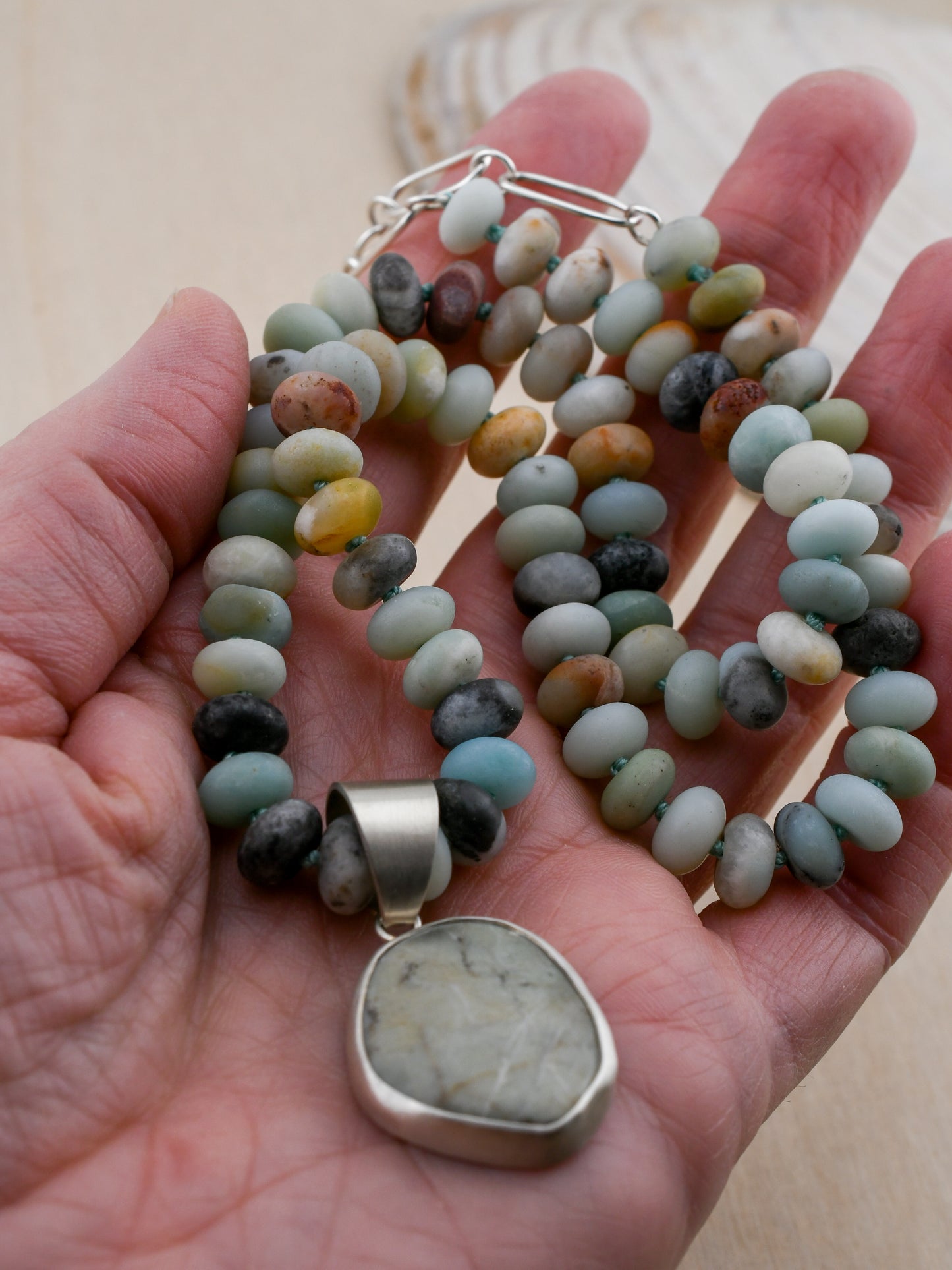 Hand holding a necklace with a pendant featuring multicolored beads and a large stone pendant.